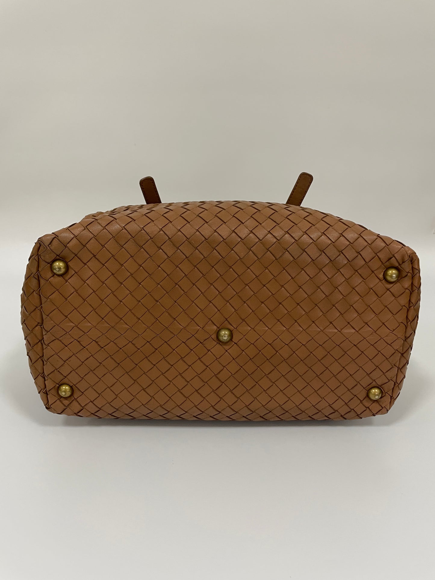 Bottom view of a Bottega Veneta Intrecciato Montaigne bag in brown leather showing the woven pattern and brass feet for protection.