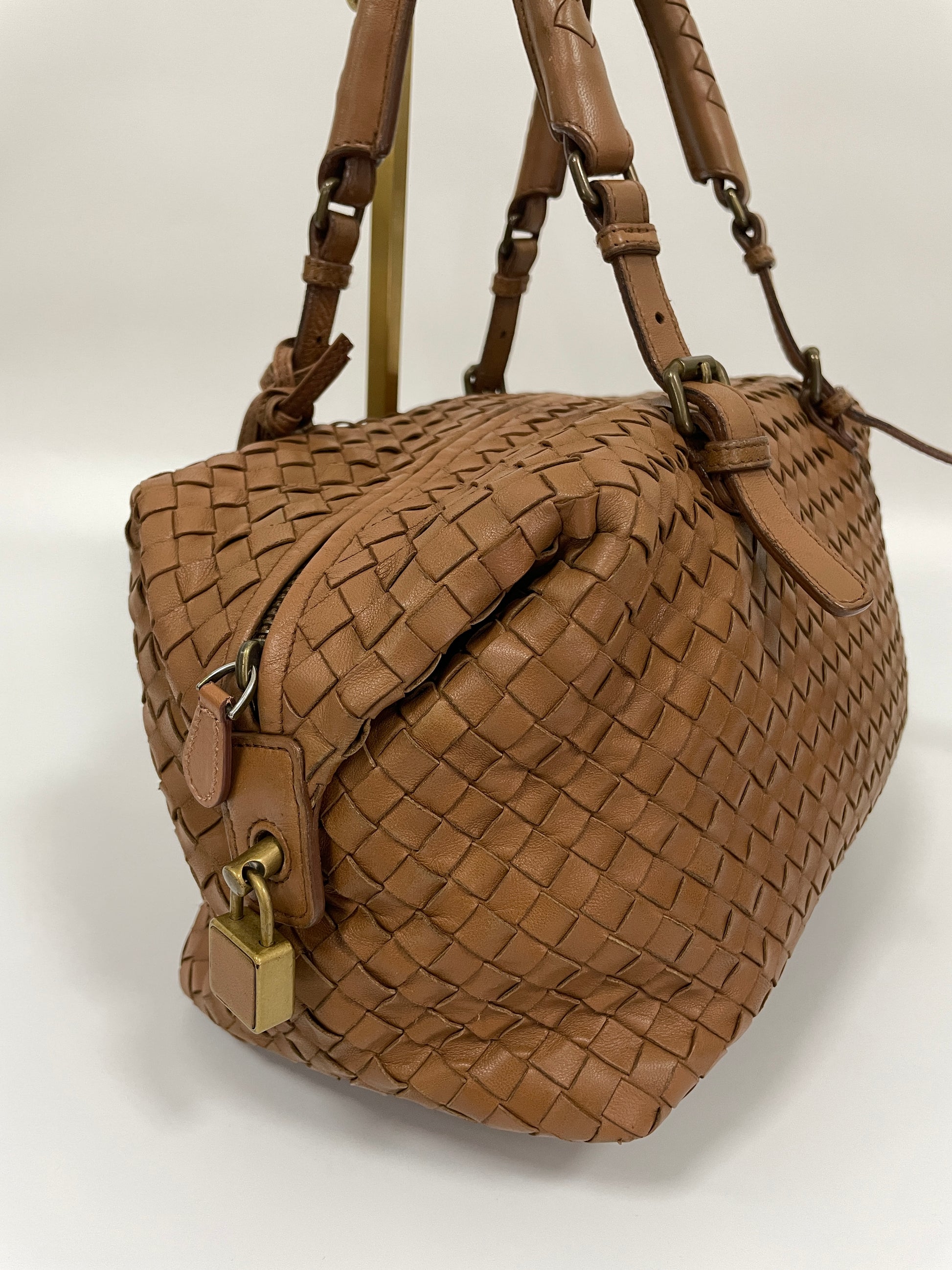 Close up side view of a Bottega Veneta Intrecciato Montaigne bag in brown leather featuring a zipper and a brass lock detail.