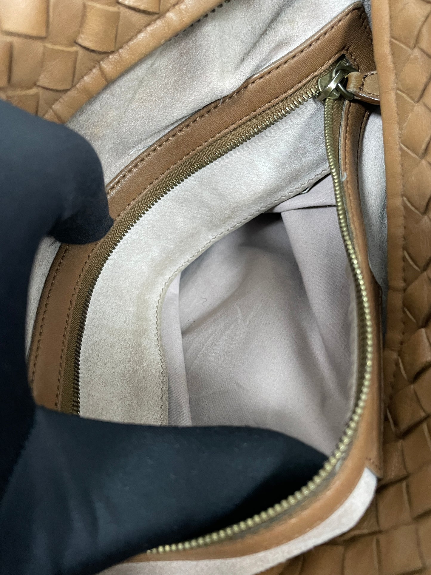 Interior view of the small zipper compartment of Bottega Veneta Intrecciato Montaigne bag in brown leather showing the spacious beige lining and zipper compartment.