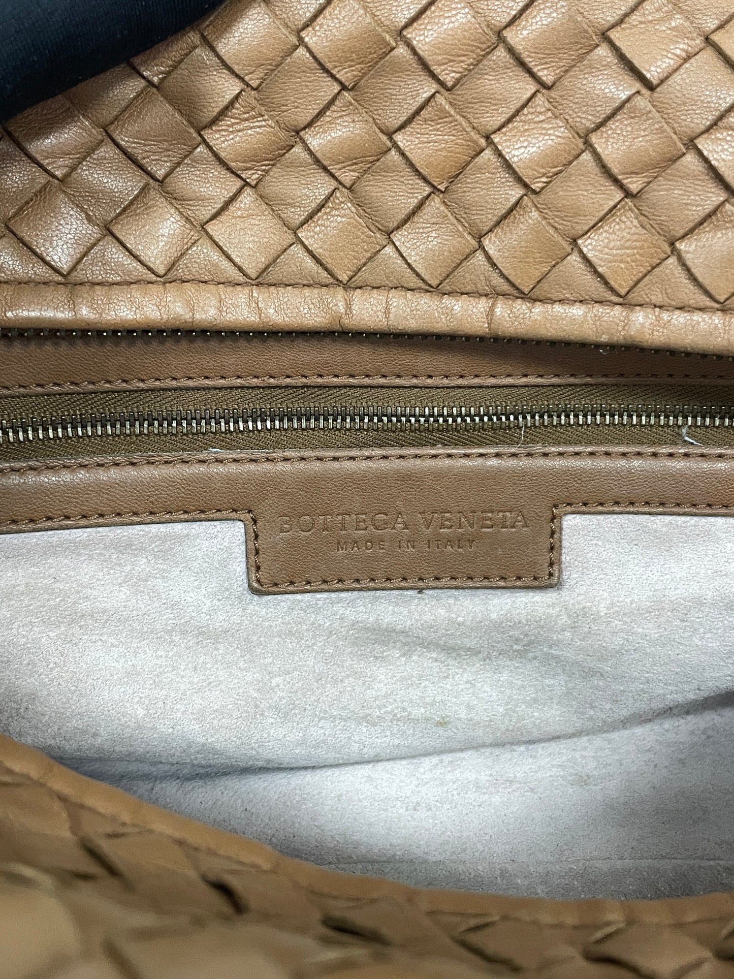 Close-up view of the interior leather label of the Bottega Veneta Intrecciato Montaigne bag in brown leather, showing "Bottega Veneta Made in Italy."