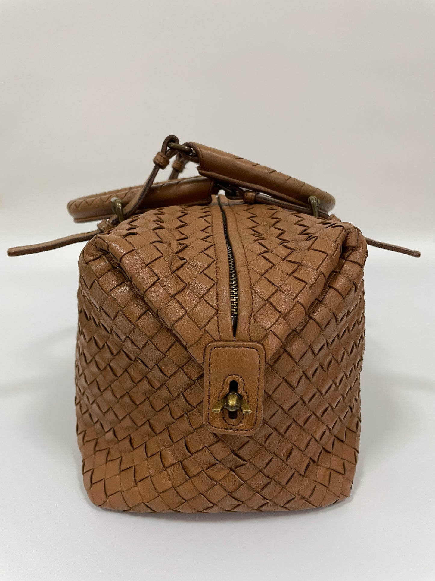 Side view of a Bottega Veneta Intrecciato Montaigne bag in brown leather featuring a zipper and a brass lock detail.