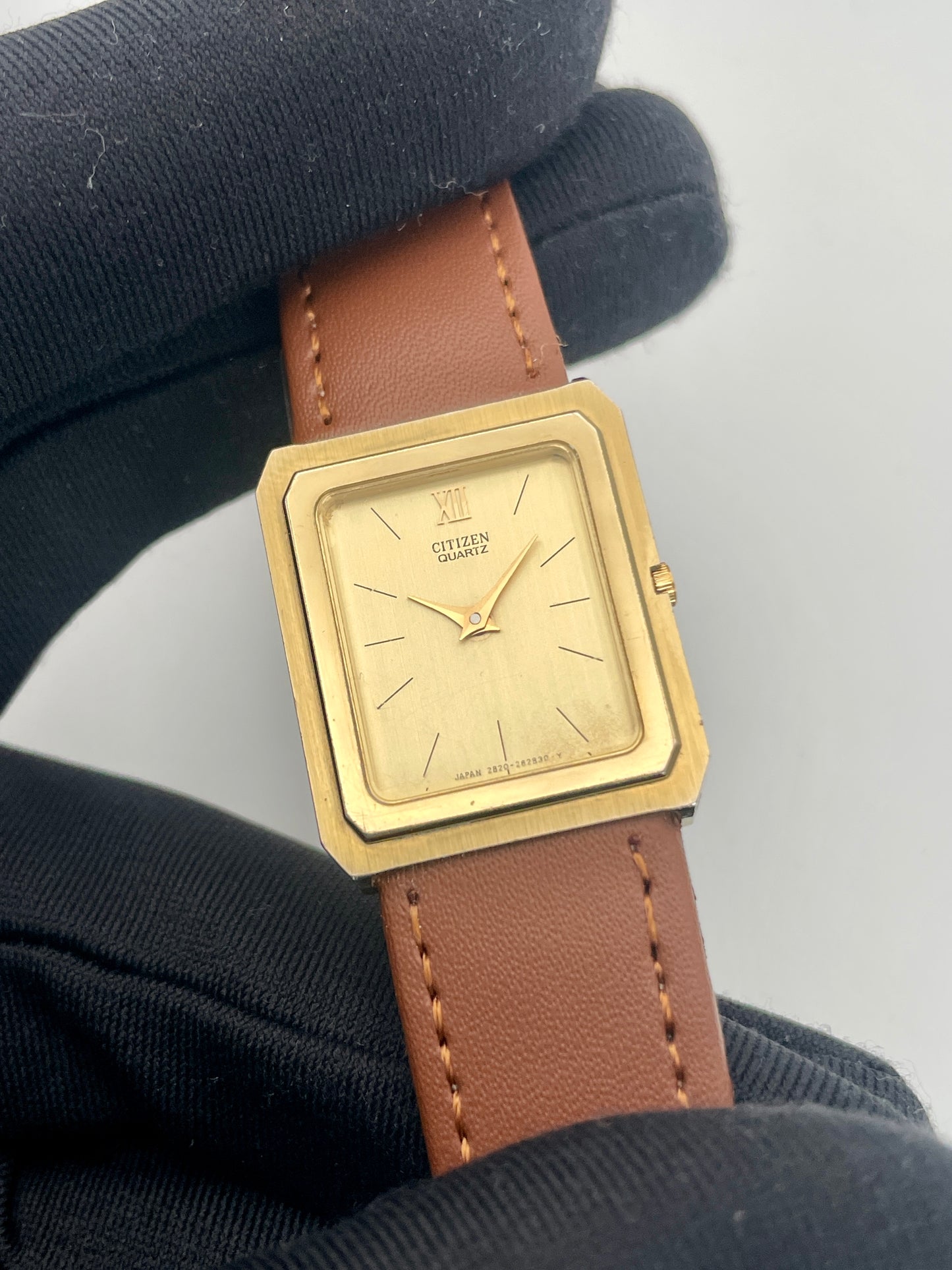 Close-up of Citizen Tank Vintage Watch in a gloved hand, showing the gold dial and brown leather strap.