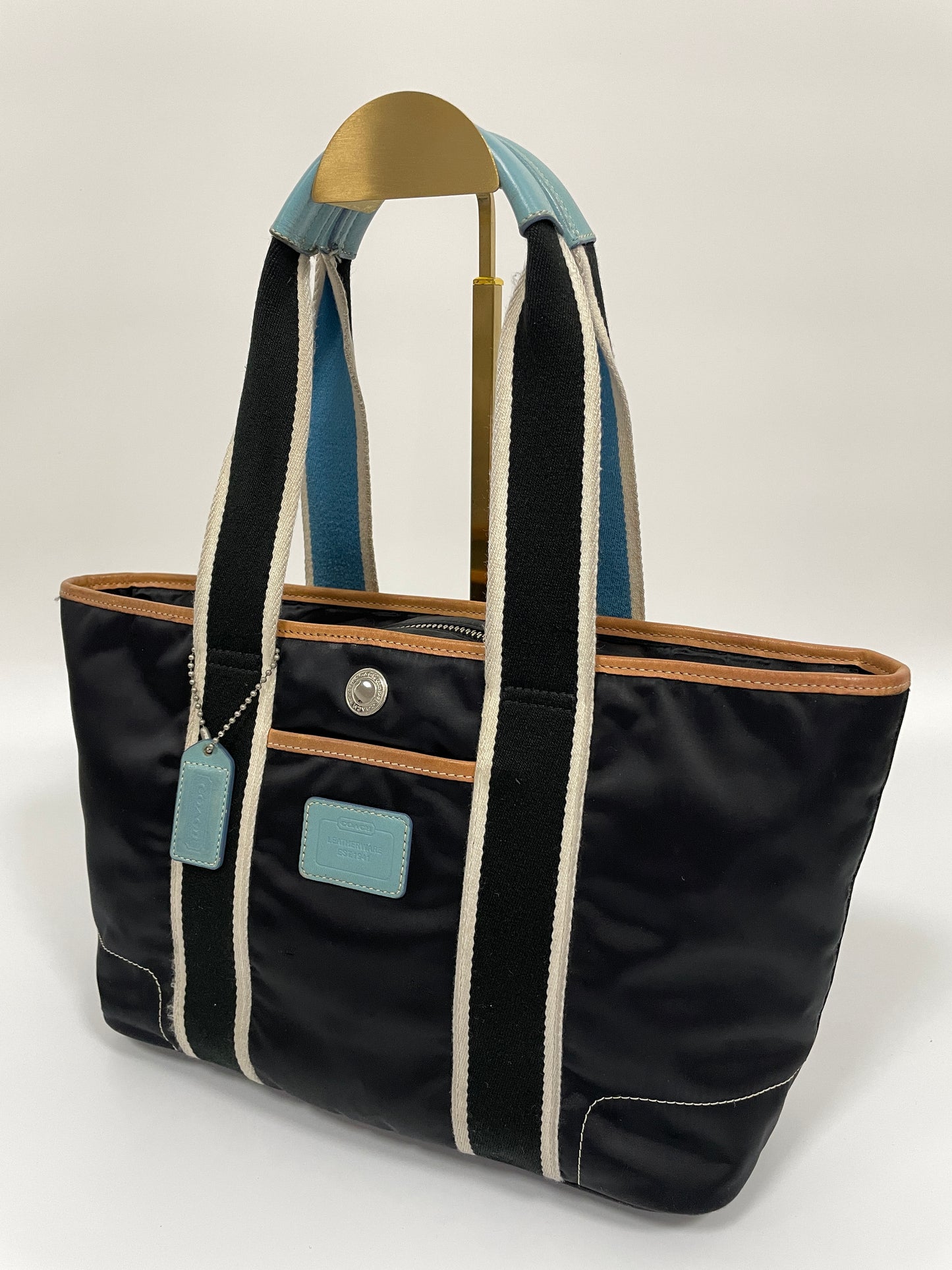 Angled view of a Coach Hampton tote bag in dark navy with contrasting white and blue handles, and light blue leather details.