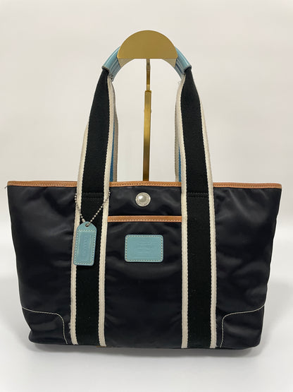 Front view of a Coach Hampton tote bag in dark navy with contrasting white and blue handles, and light blue leather details.