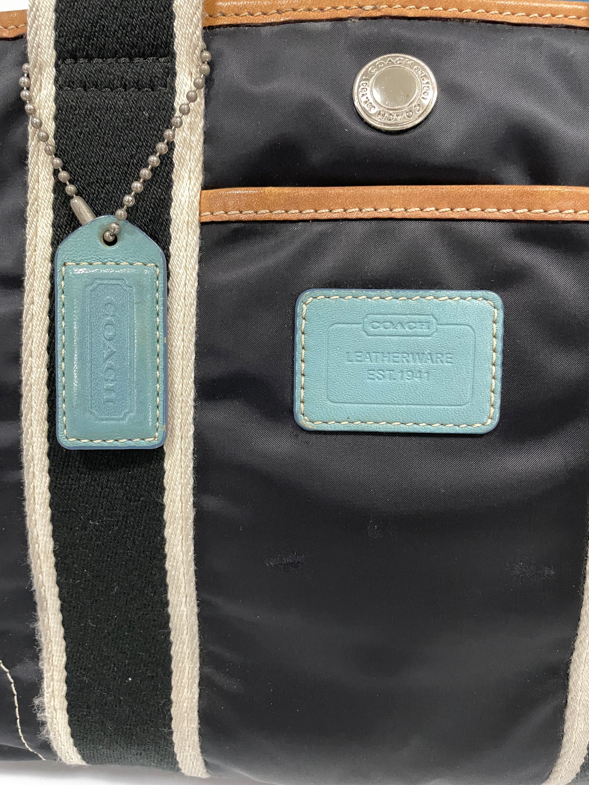 Close-up of the Coach logo tag on the dark navy Hampton tote bag with light blue leather accents.