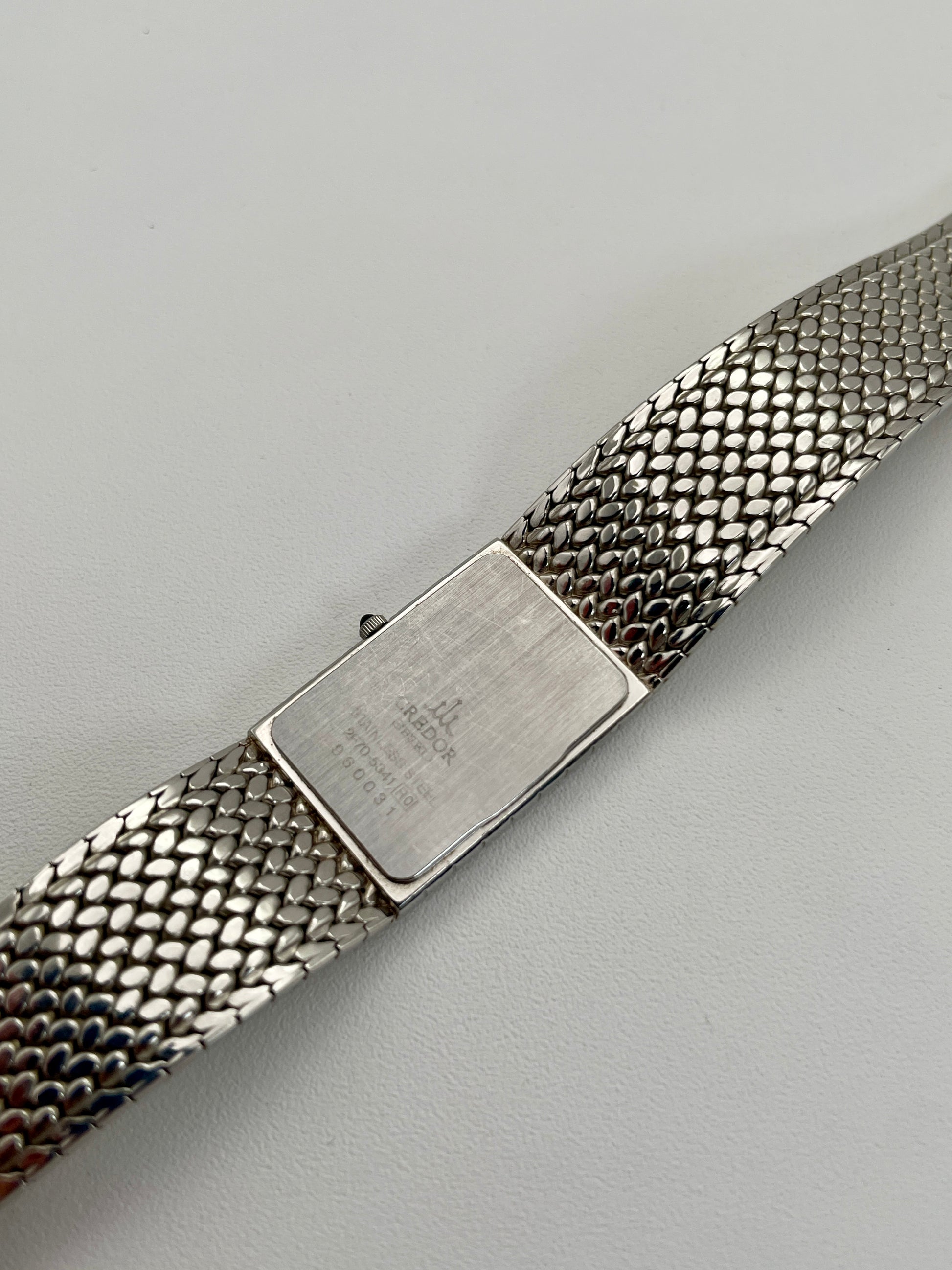 Caseback view of a Credor 2F70 bracelet watch, displaying the engraved details on the silver-tone caseback and the unique mesh bracelet design.