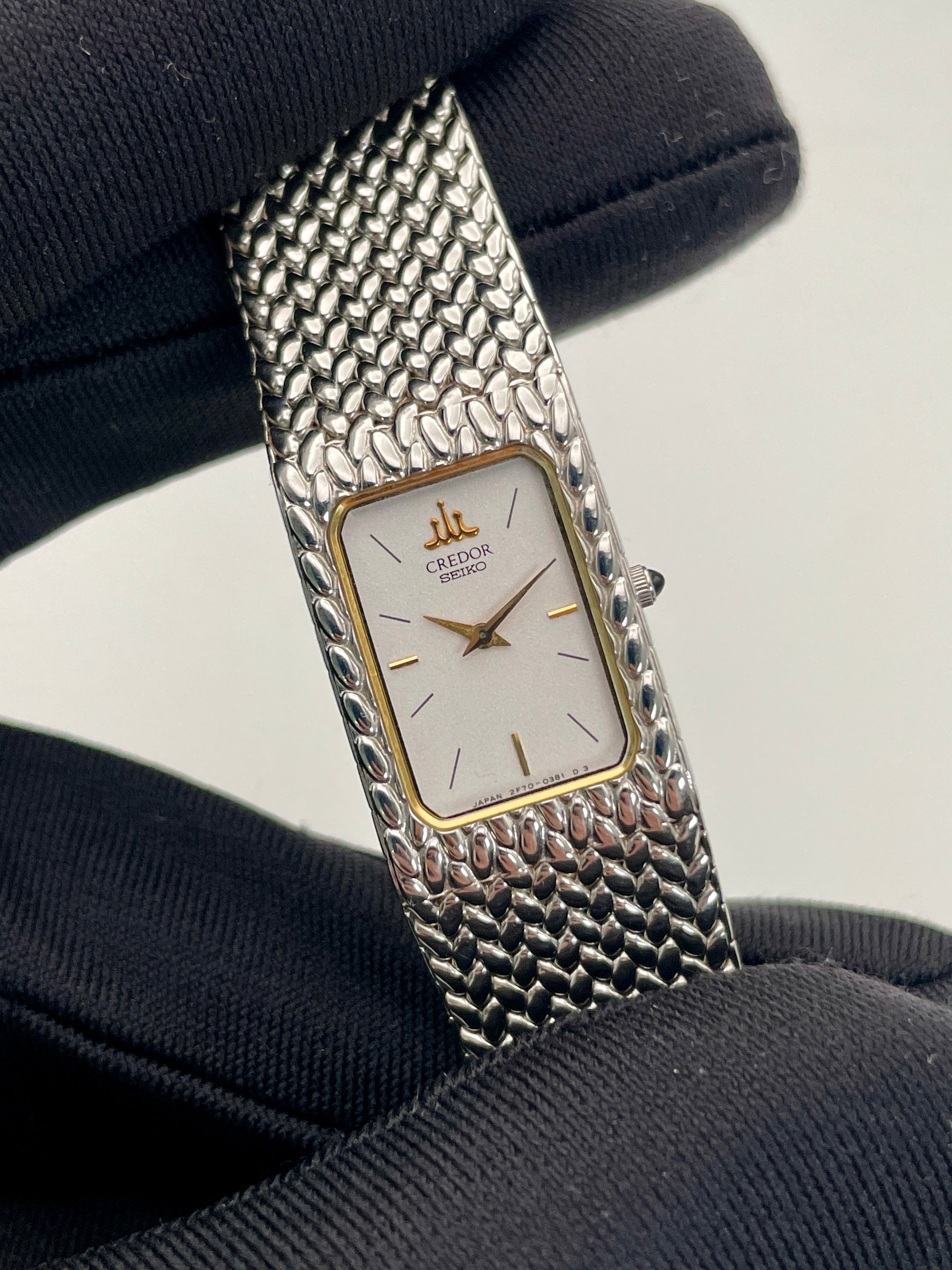 Close-up view of a Credor 2F70 bracelet watch, focusing on the silver-tone rectangular case, gold-tone bezel, white dial, and the finely detailed mesh bracelet.