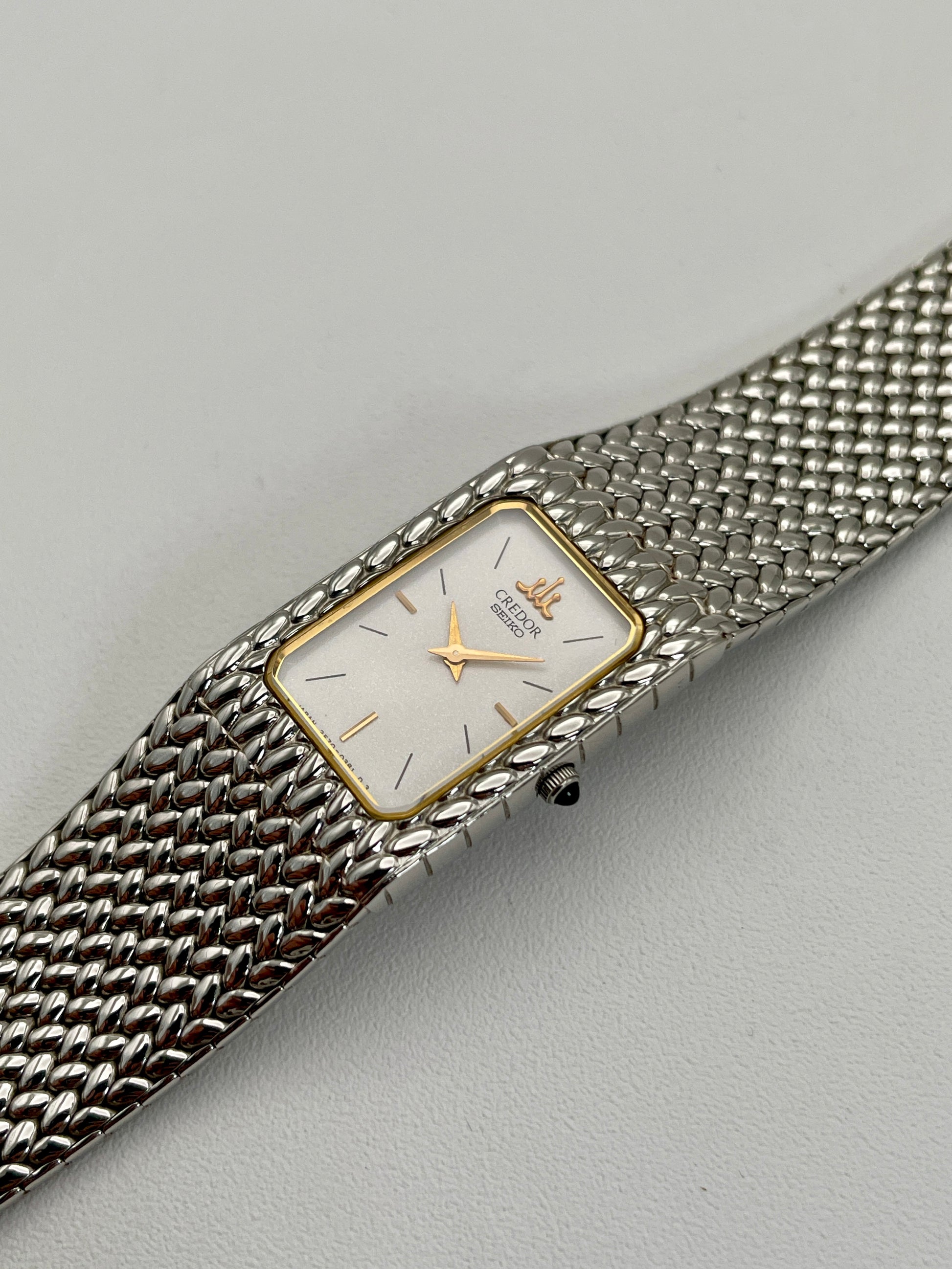 Diagonal view of a Credor 2F70 bracelet watch, highlighting the silver-tone rectangular case with a gold-tone bezel, white dial, and the intricately designed mesh bracelet.