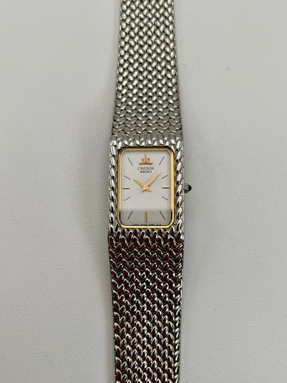 Front view of a Credor 2F70 bracelet watch featuring a rectangular silver-tone case with a gold-tone bezel, white dial, and silver-tone mesh bracelet with a unique textured pattern.