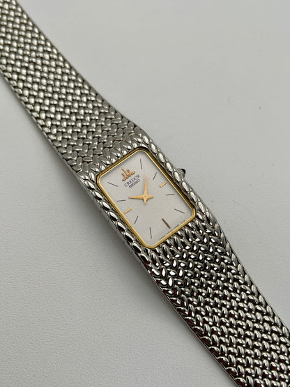 View of a Credor 2F70 bracelet watch featuring a rectangular silver-tone case with a gold-tone bezel, white dial, and silver-tone mesh bracelet with a unique textured pattern.