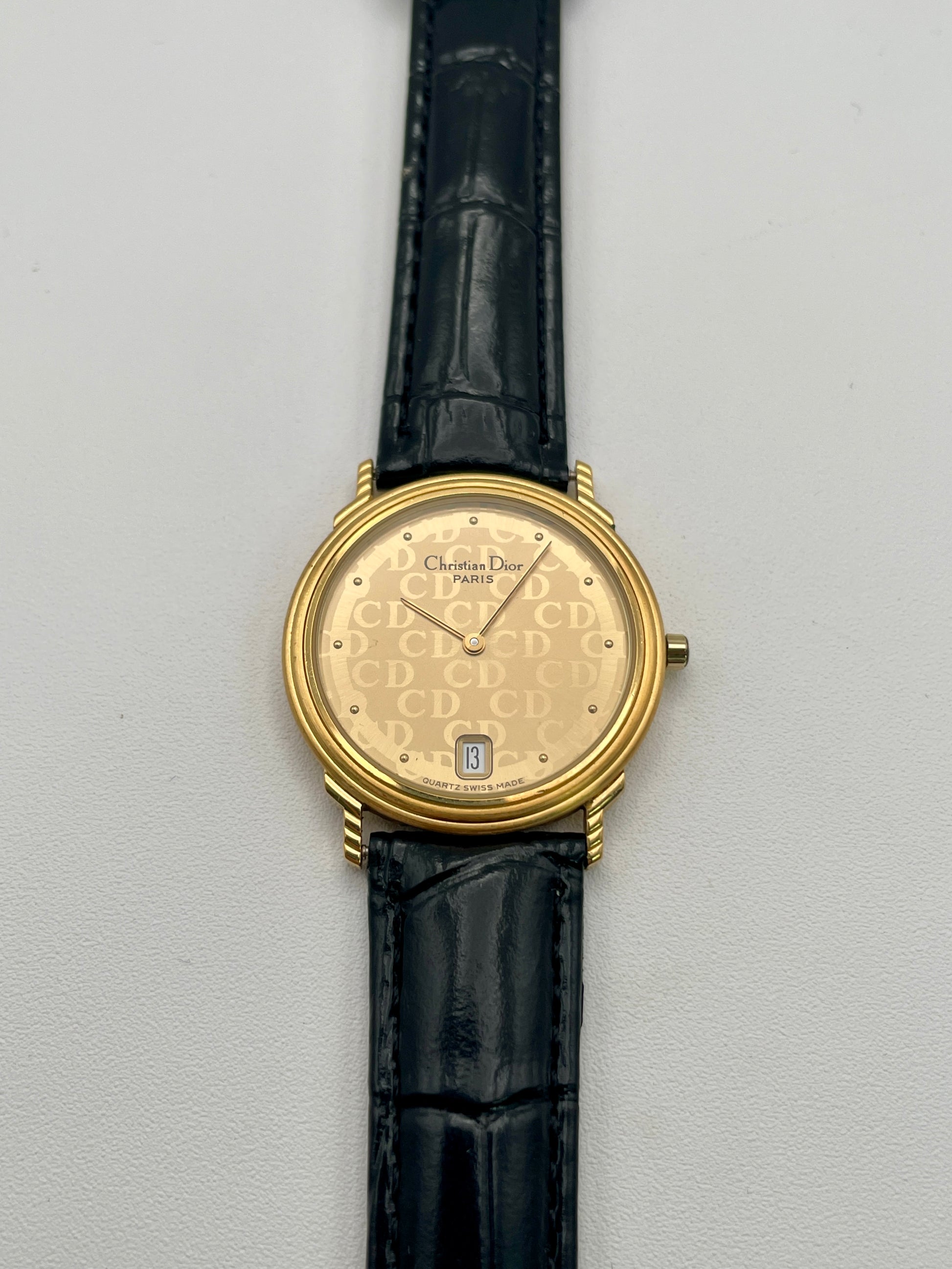 Christian Dior 45.122 vintage women's watch in gold-tone case with CD monogram dial and black leather strap, front view
