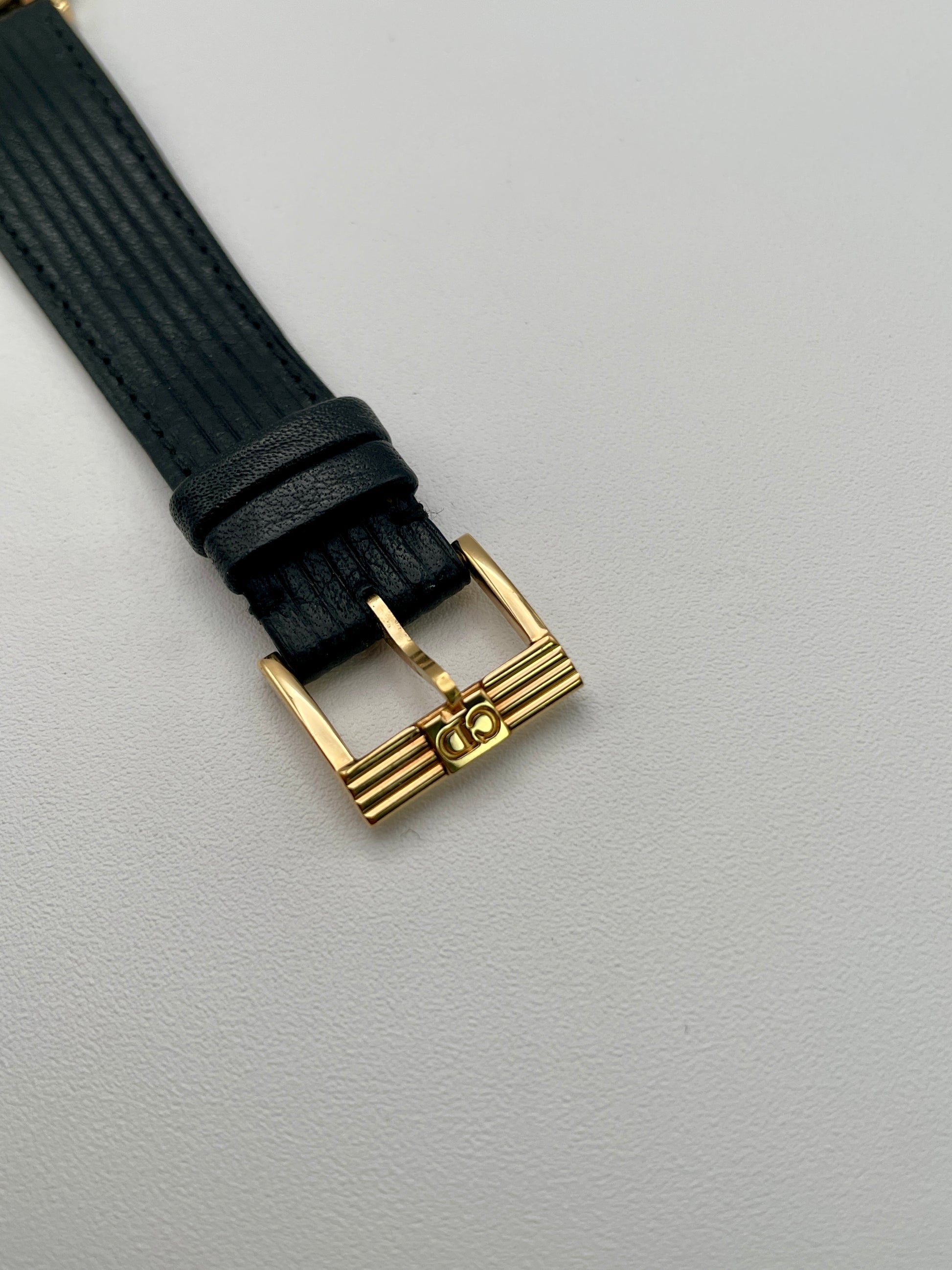 Buckle detail of black ribbed leather strap with gold Dior initials
