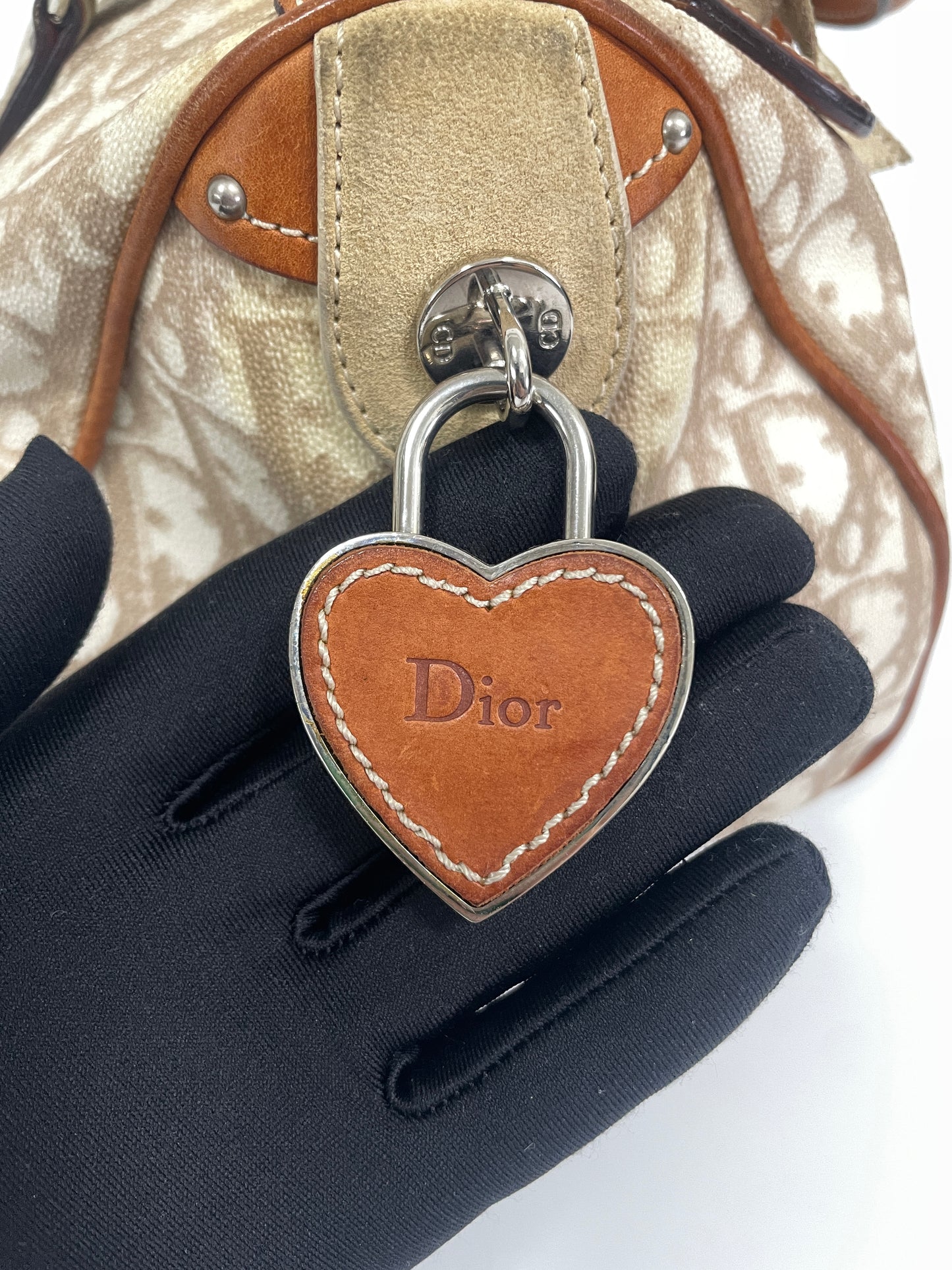 Close-up of the heart-shaped Dior leather charm on the Christian Dior Trotter Romantique Bag in beige leather and canvas.