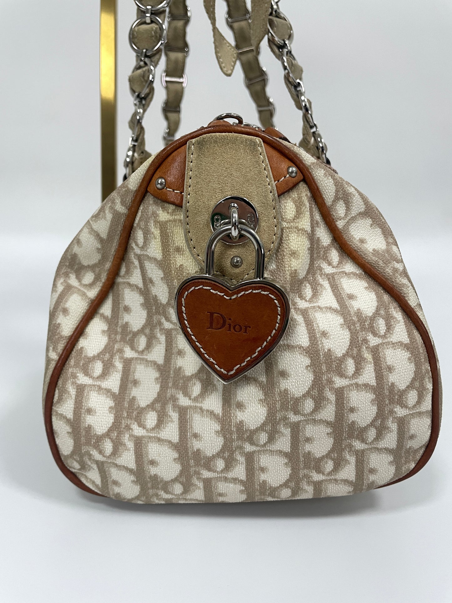 Side view of the Christian Dior Trotter Romantique Bag in beige leather and canvas, featuring a brown leather heart-shaped Dior charm.