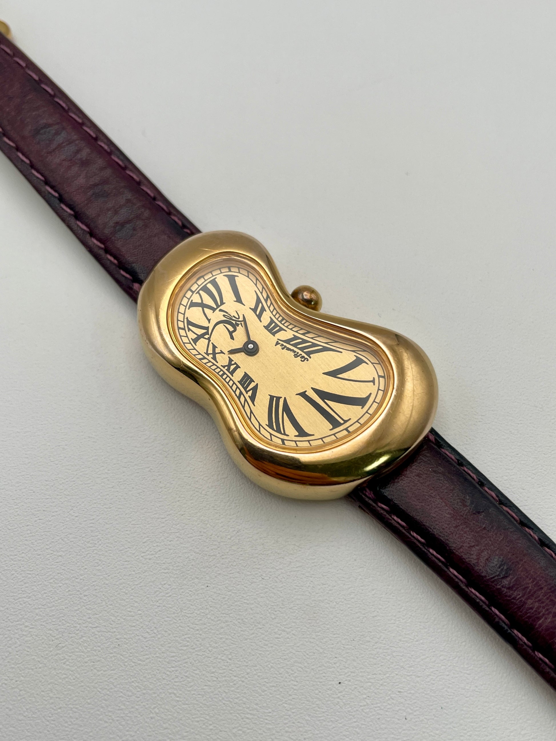 Exaequo Salvador Dali Softwatch vintage watch in gold with a surreal melted case and burgundy leather strap, front view.
