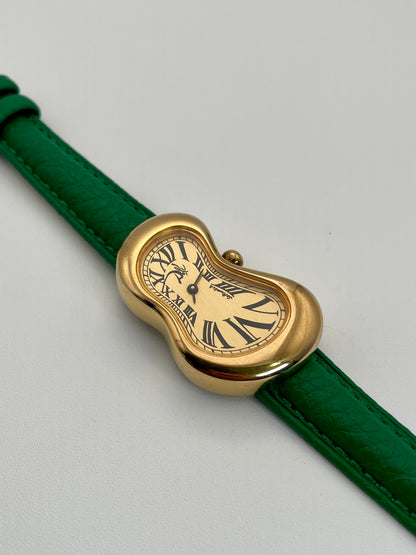 Exaequo Salvador Dali Softwatch with a gold-toned, distorted case, Roman numeral dial, and green leather strap.