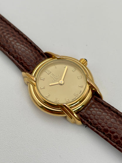 Fendi 300L watch featuring a gold-tone case, Roman numeral dial, and brown leather strap.