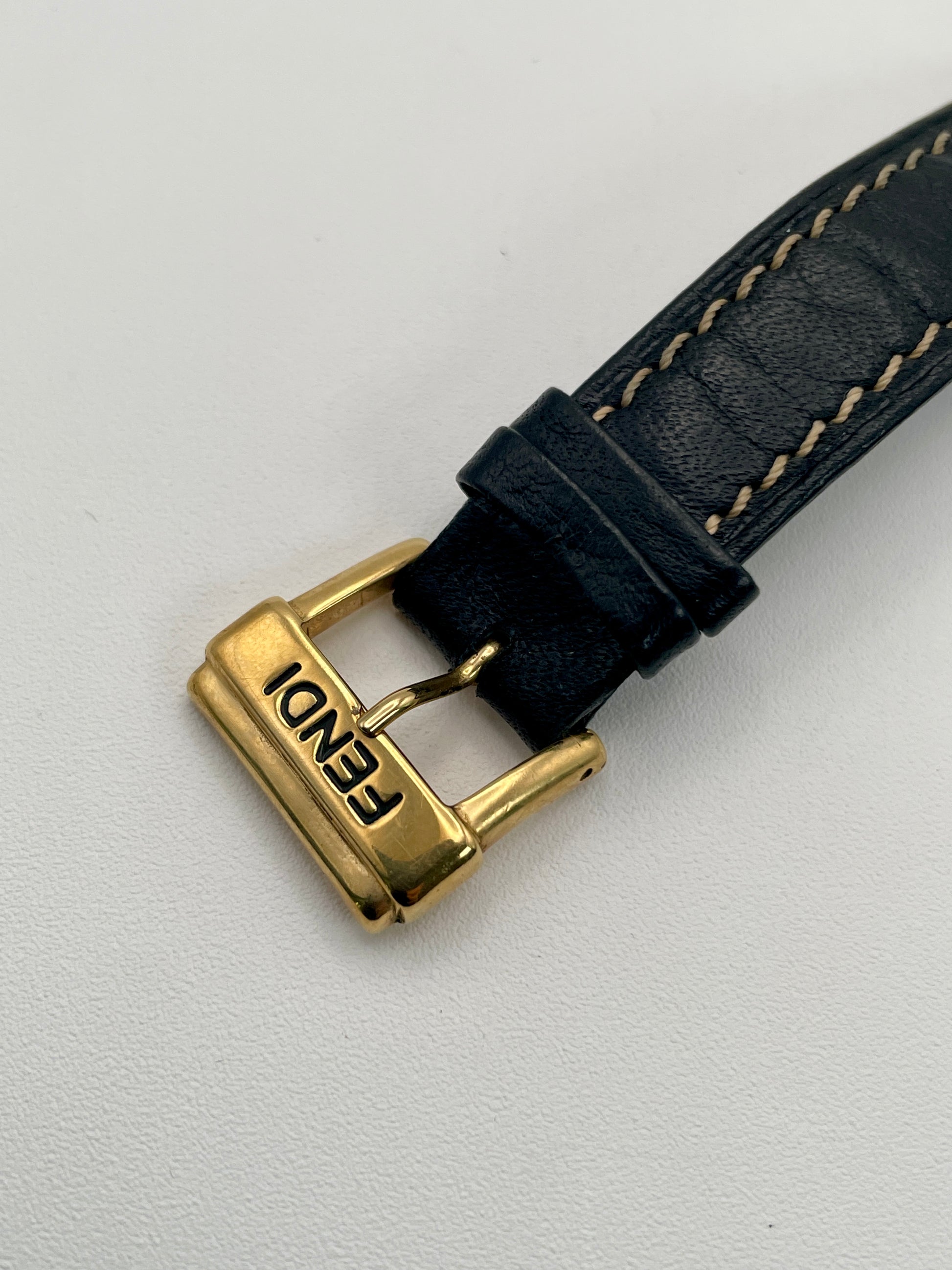 Close-up of the signed Fendi gold-tone buckle attached to the textured black leather strap.