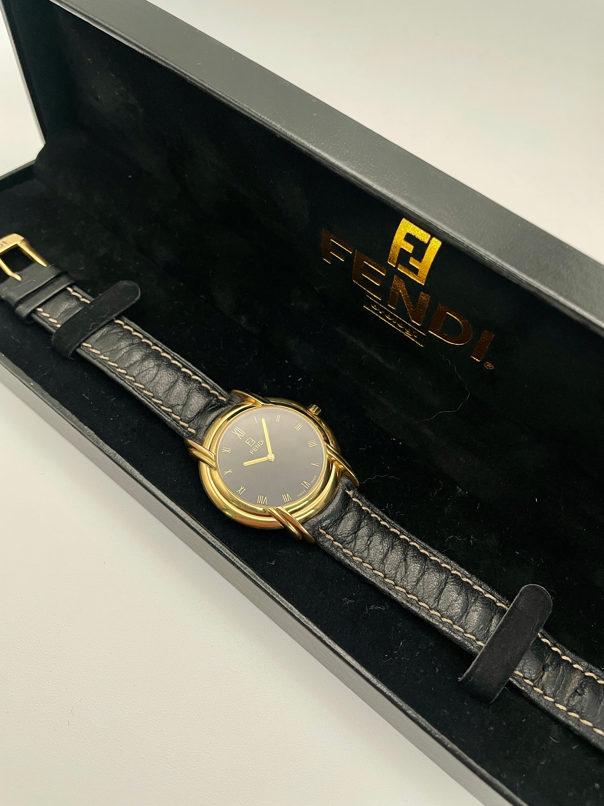 Fendi 300J vintage watch in gold-tone case with black dial and leather strap, displayed in original Fendi box.