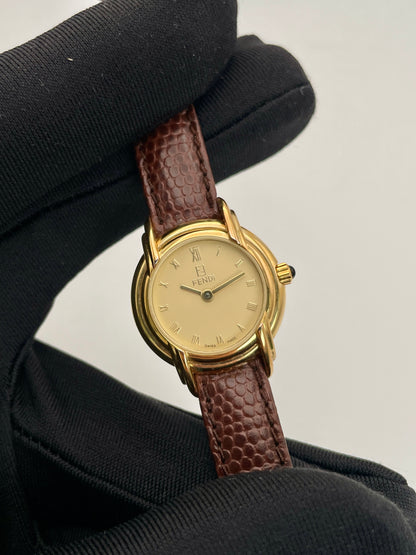 Close-up view of Fendi 300L watch with a gold-tone case, Roman numeral dial, and brown leather strap.