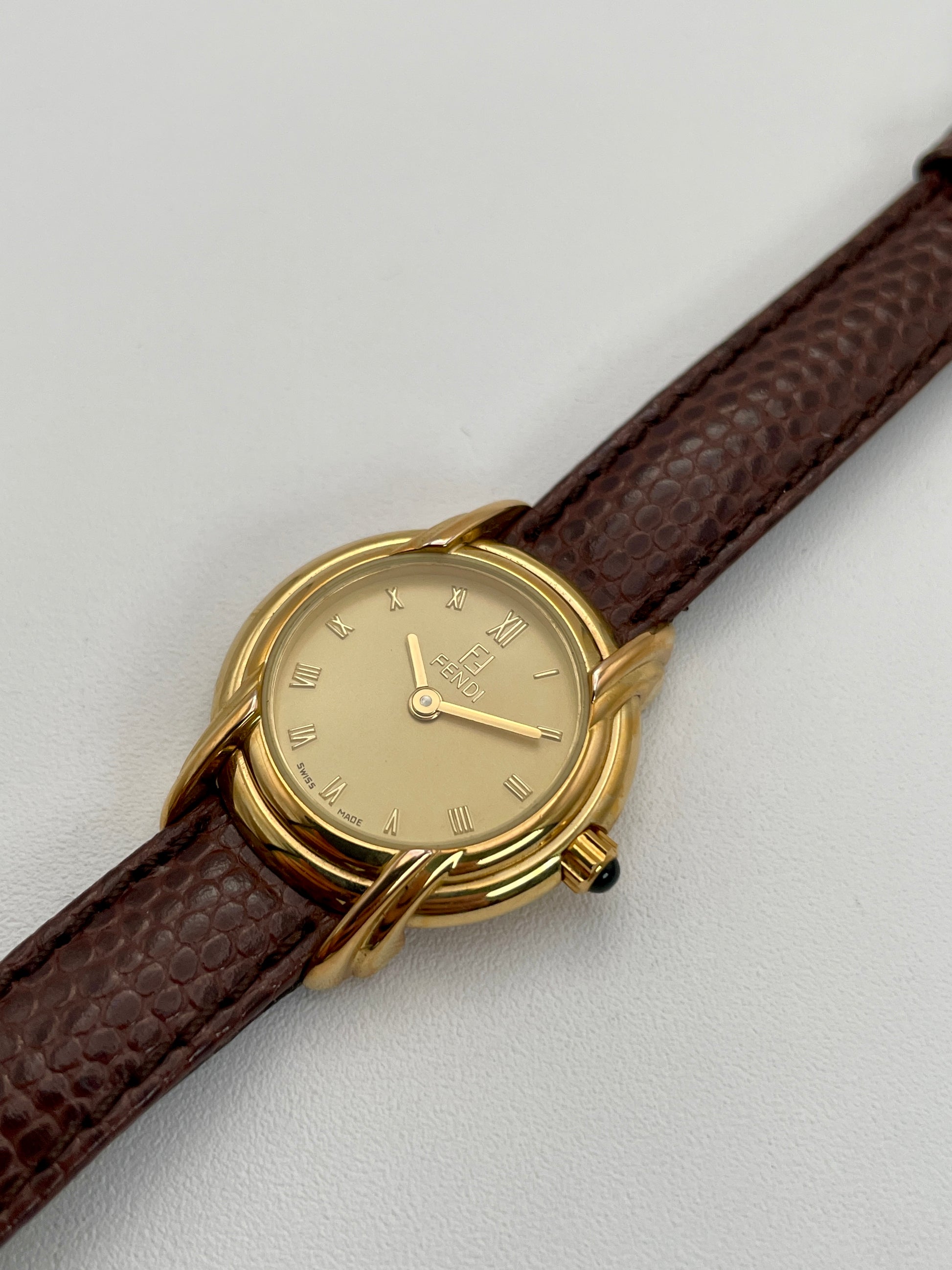 Diagonal view of Fendi 300L watch with a gold-tone case, Roman numeral dial, and brown leather strap.