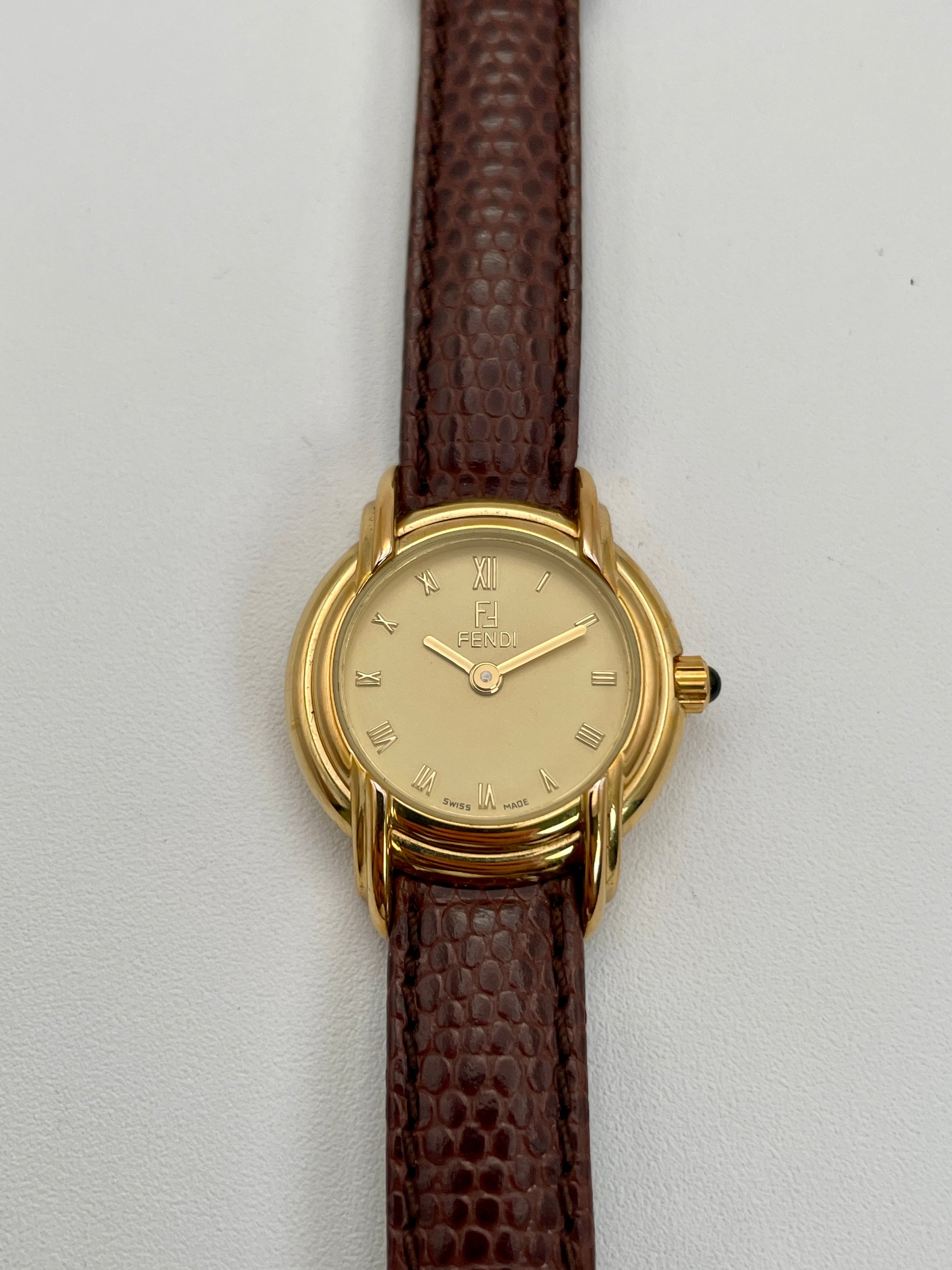 Front view of Fendi 300L watch featuring a gold-tone case, Roman numeral dial, and brown leather strap.