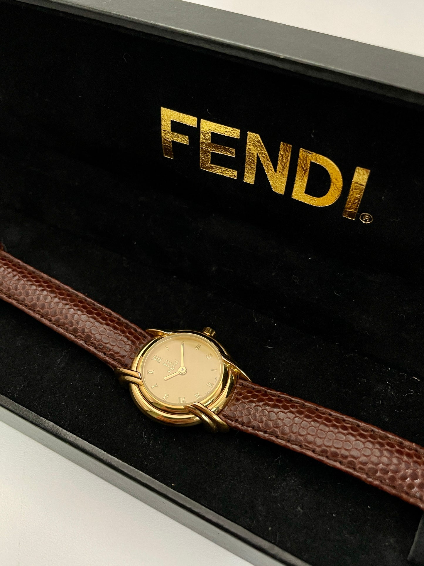 Fendi 300L watch with gold-tone case and brown leather strap, displayed in a black Fendi box.