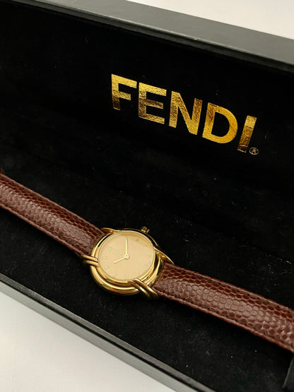 Fendi 300L watch with gold-tone case and brown leather strap, displayed in a black Fendi box.