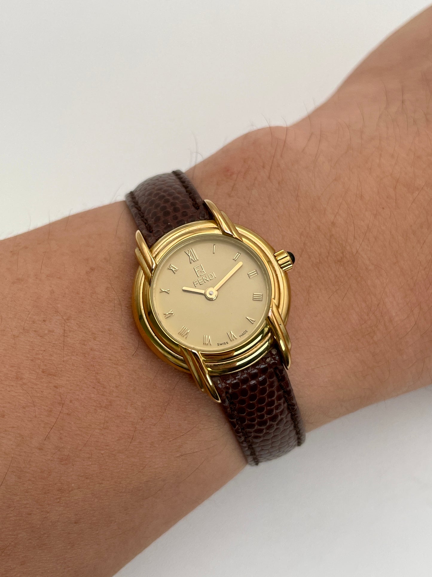 Fendi 300L watch worn on wrist, featuring a gold-tone case, Roman numeral dial, and brown leather strap.