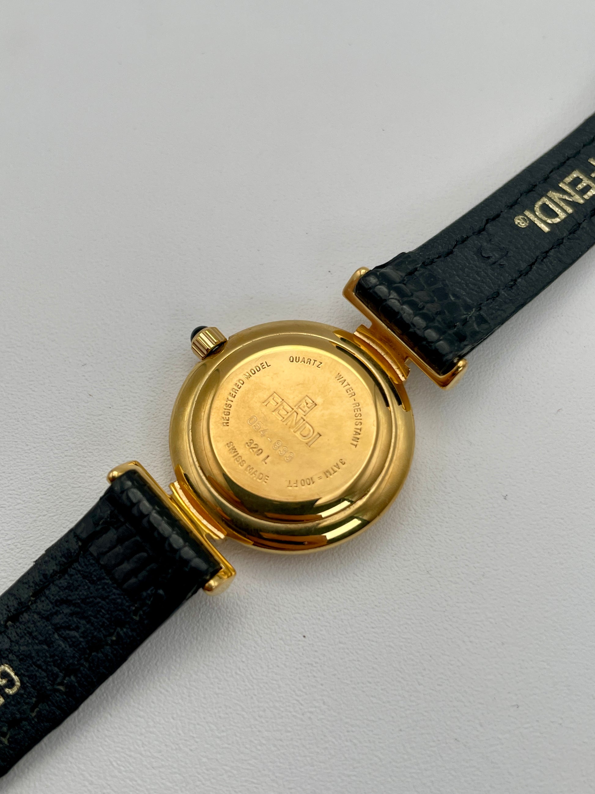 Caseback view of the Fendi 320L watch with a gold-tone round case and black leather strap