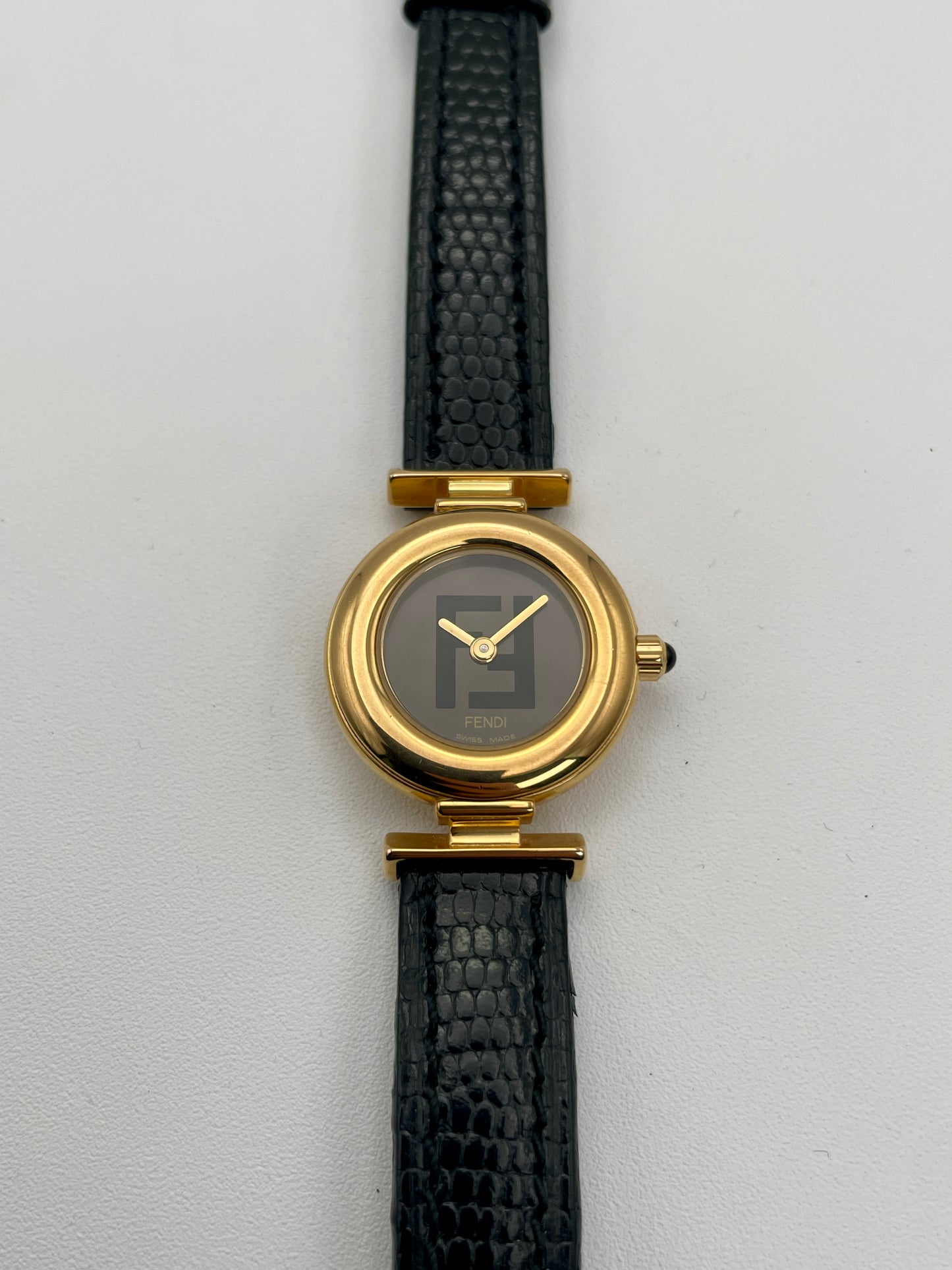 Front view of the Fendi 320L watch with a gold-tone round case, black leather strap, and black dial with Fendi logo