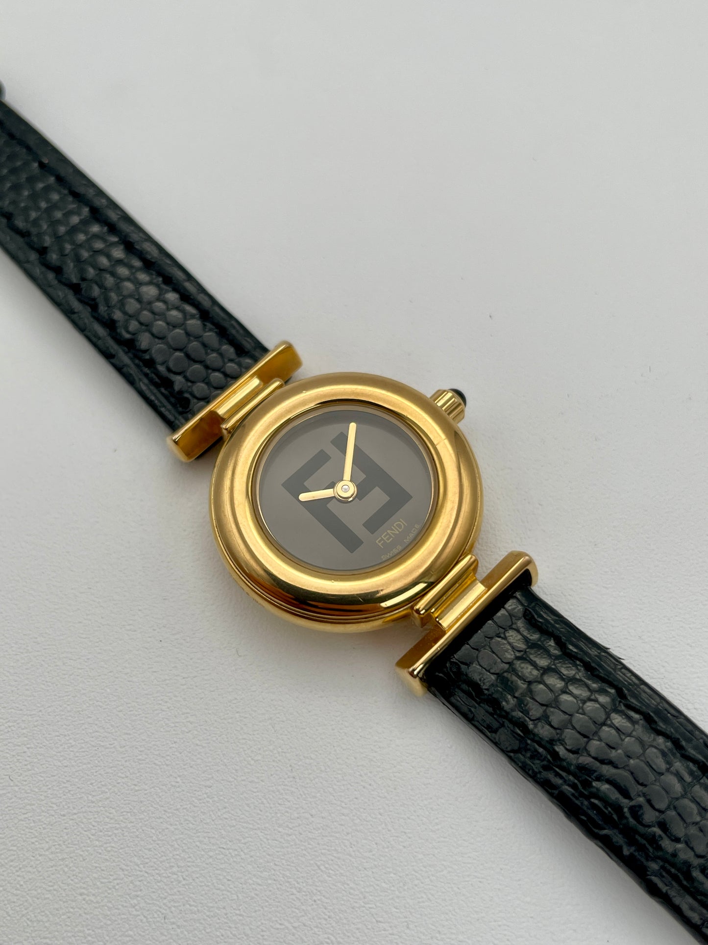 Fendi 320L watch featuring a gold-tone round case, black leather strap, and black dial with Fendi logo
