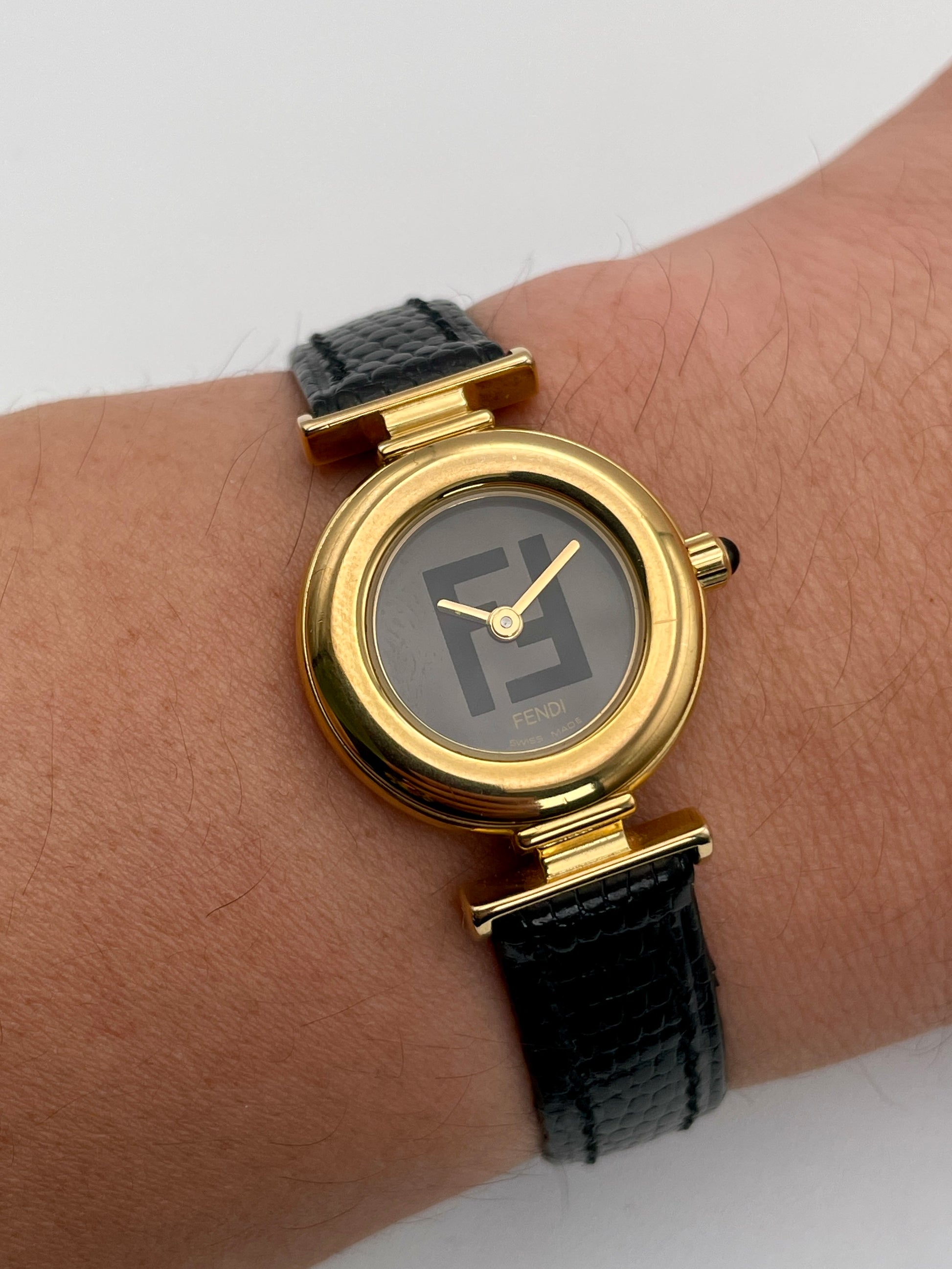 Fendi 320L watch worn on wrist, showcasing the gold-tone round case, black dial with Fendi logo, and black leather strap.