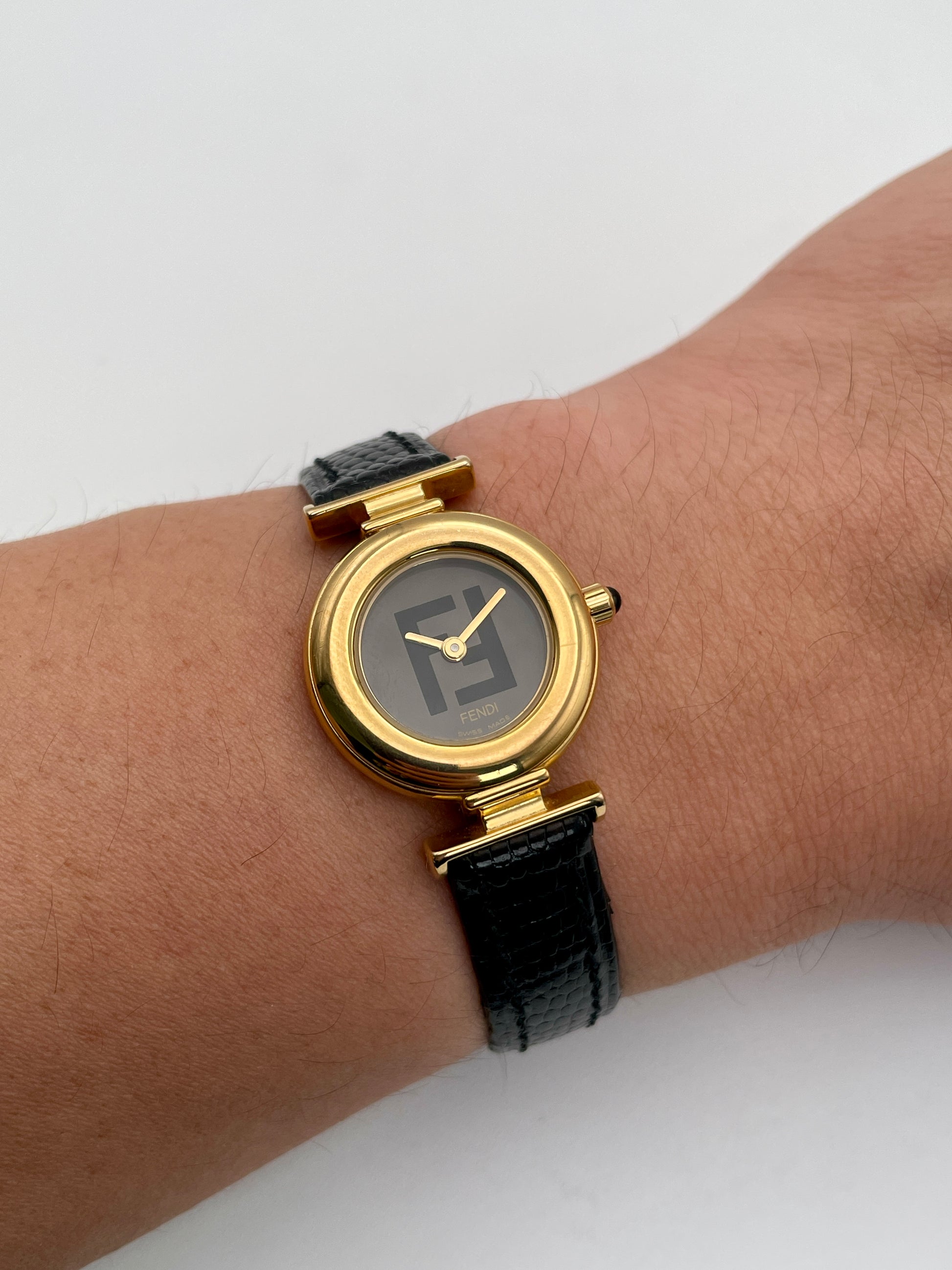 Fendi 320L watch worn on wrist, showcasing the gold-tone round case, black dial with Fendi logo, and black leather strap