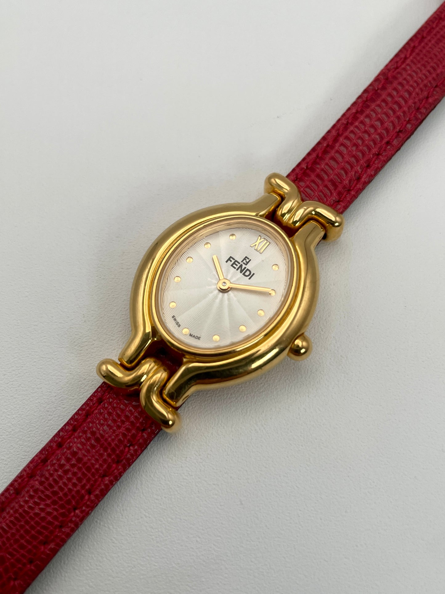 Angled view of the Fendi 640L gold watch featuring a white guilloché dial and red leather strap.