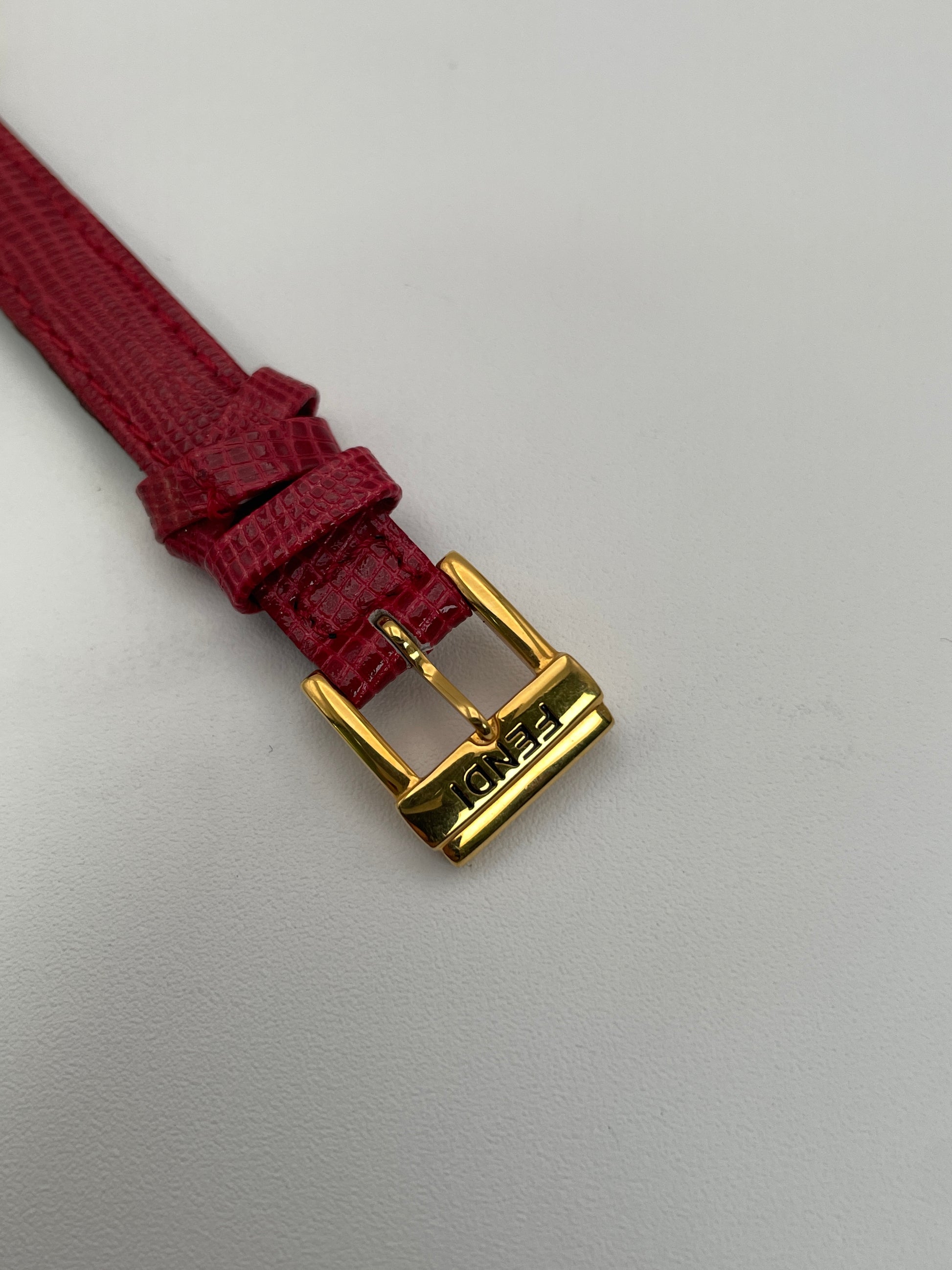 Close-up of the Fendi 640L gold-plated buckle with engraved logo on a red leather strap.