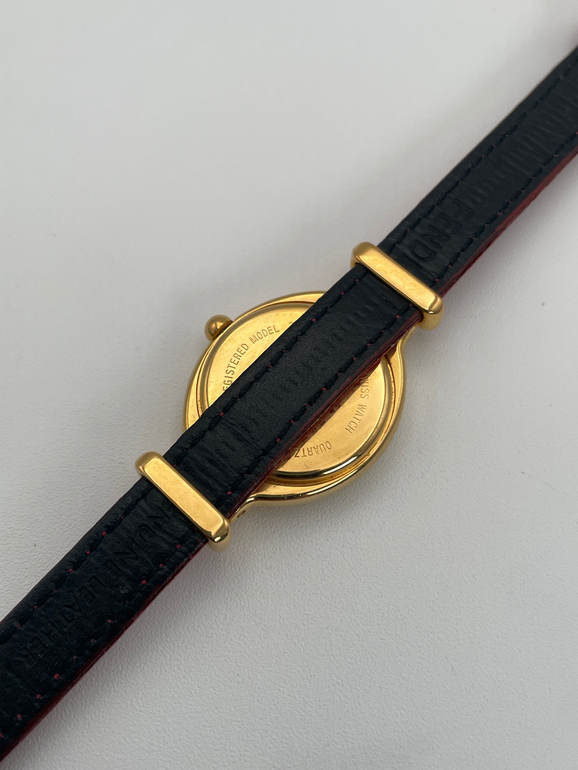 Caseback view of the Fendi 640L gold watch with engraved details and a red leather strap.