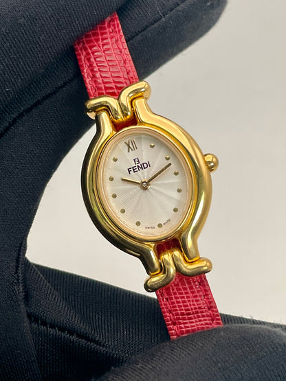 Handheld close-up of the Fendi 640L gold watch on a red leather strap, highlighting the guilloché dial.