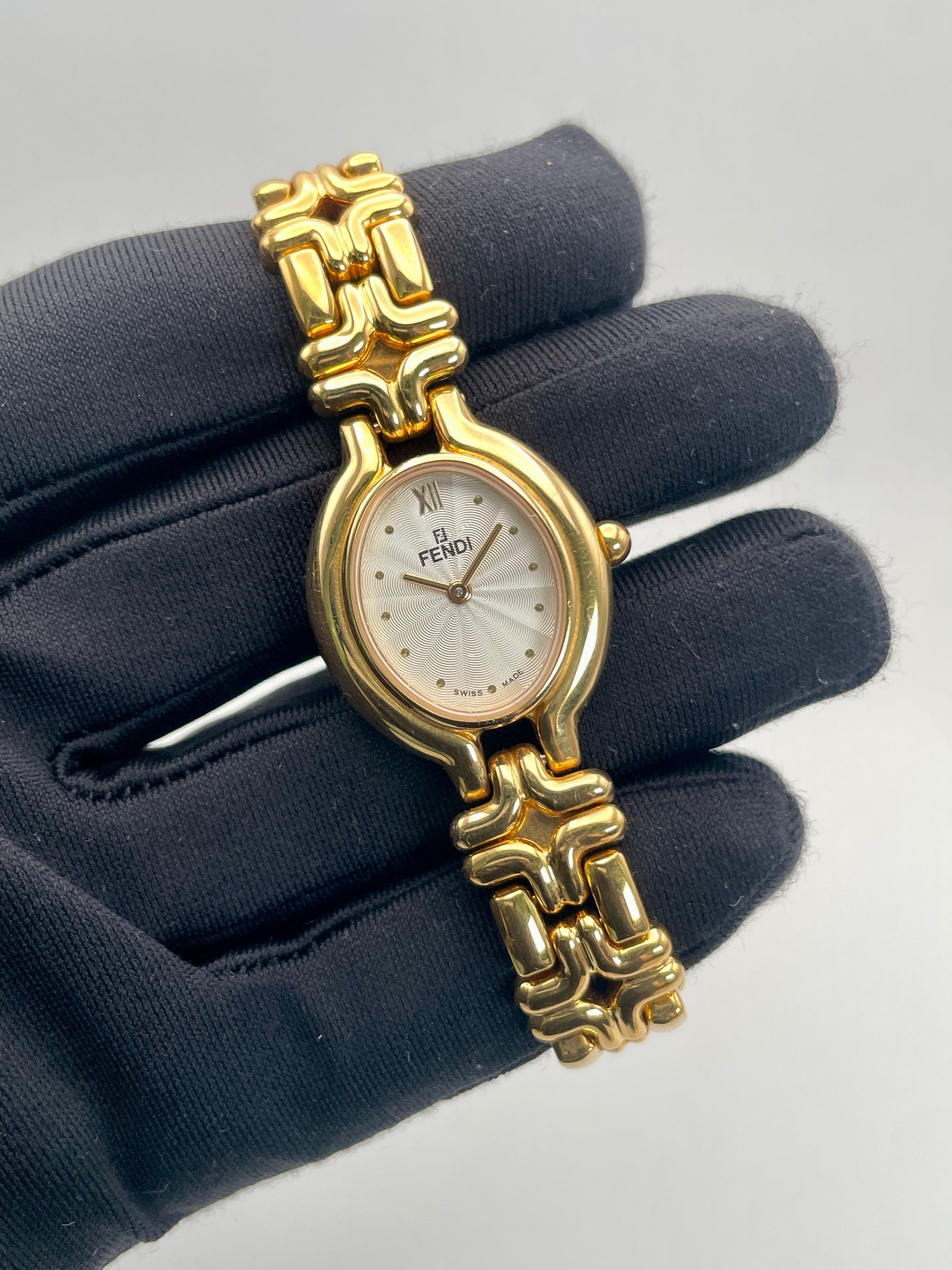 Handheld view of the Fendi 640L Vintage Women's Watch, showcasing the gold-tone oval case, guilloché dial, and sculptural bracelet.