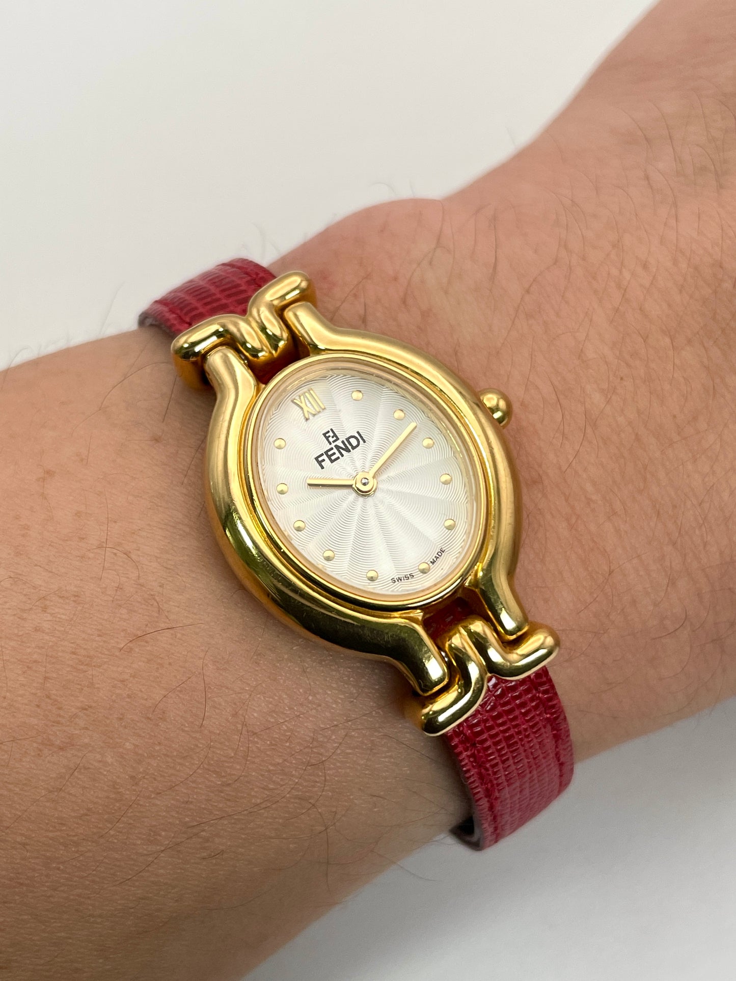 Fendi 640L gold watch worn on the wrist with a red leather strap, showcasing its elegant design.