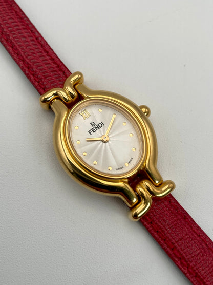 Close-up of the Fendi 640L gold watch with a guilloché dial on a red leather strap.