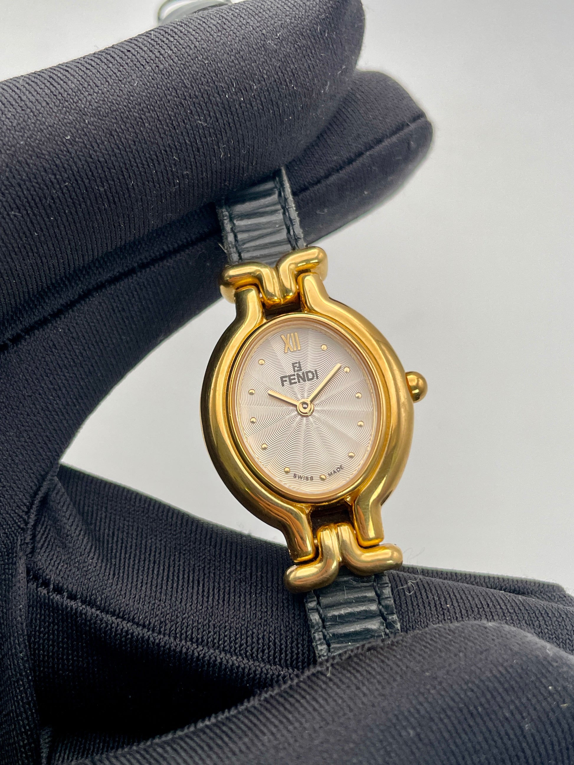 Close-up view of Fendi 640L watch's white dial, gold hands, and black leather strap.