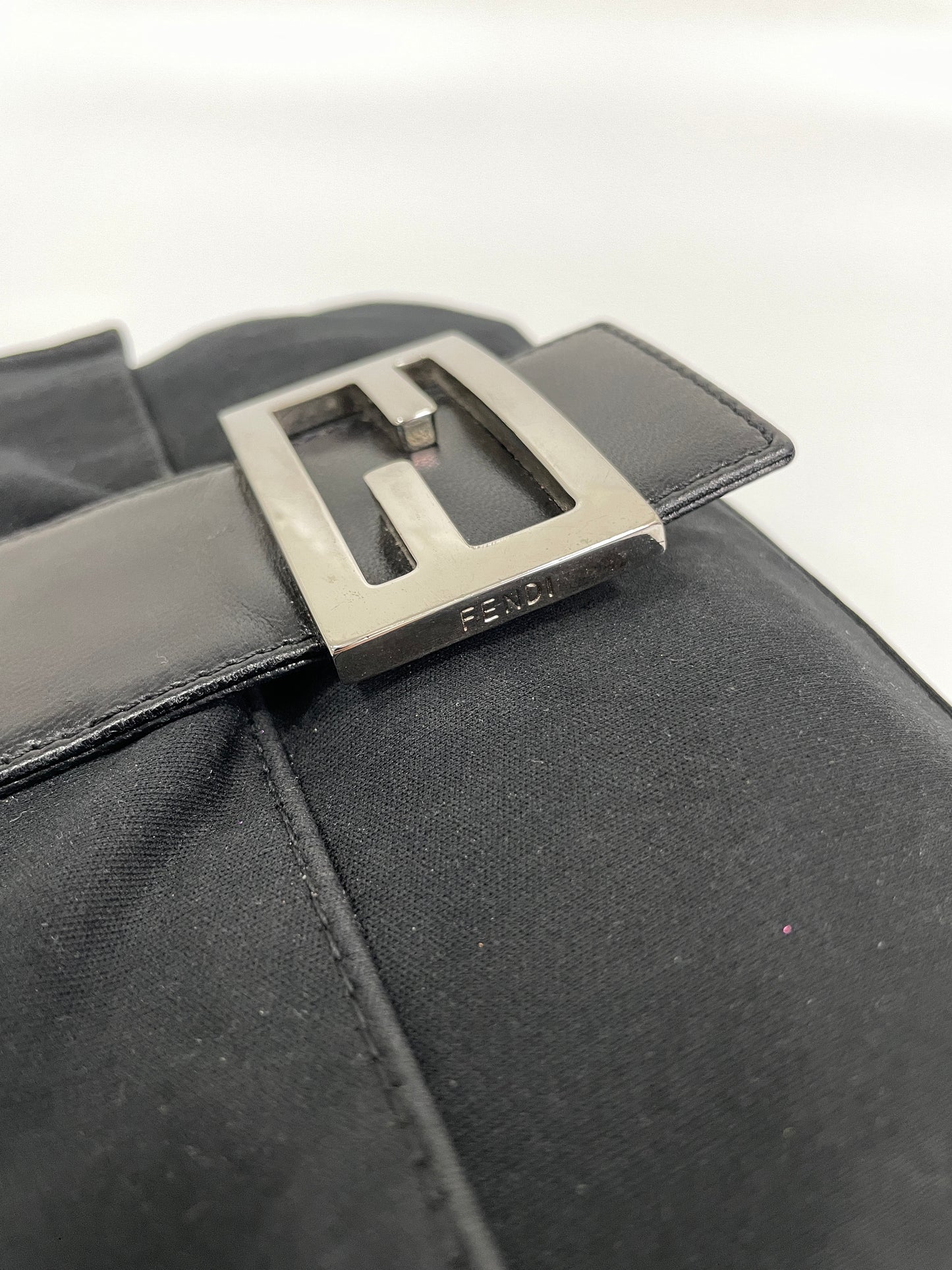 Close-up of the silver Fendi logo buckle on the Fendi Baguette Bag in black neoprene.