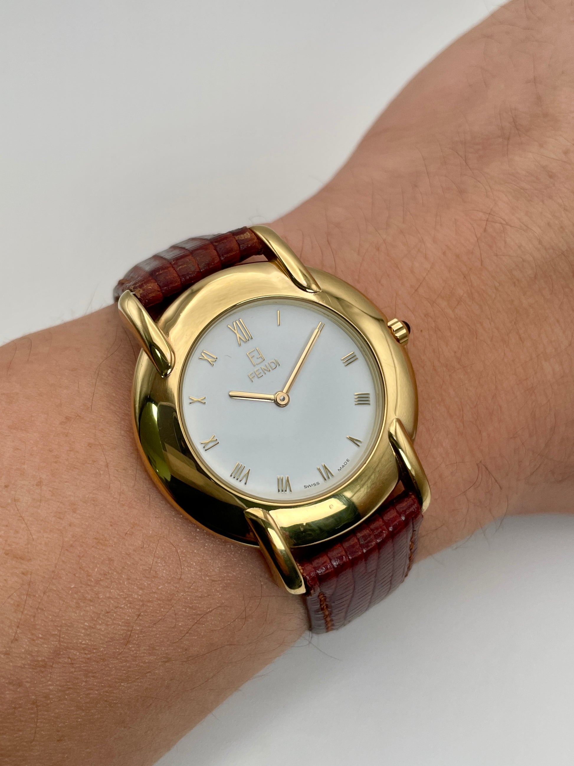 The Fendi Orologi 410G vintage watch in gold with a red leather strap worn on the wrist, showcasing its elegant design.