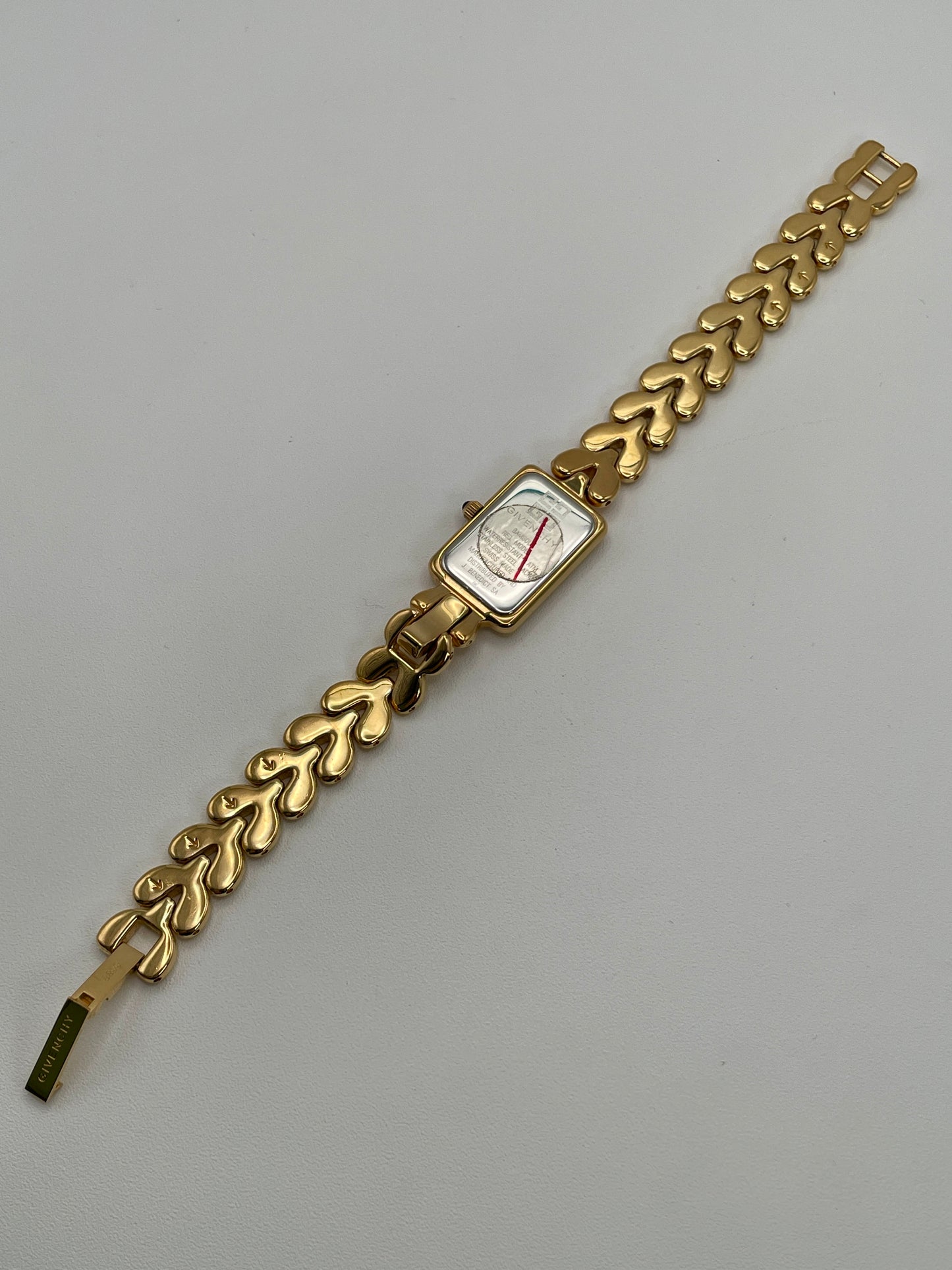 Flatlay of the Givenchy Bambou watch showing the caseback and signed bracelet in gold