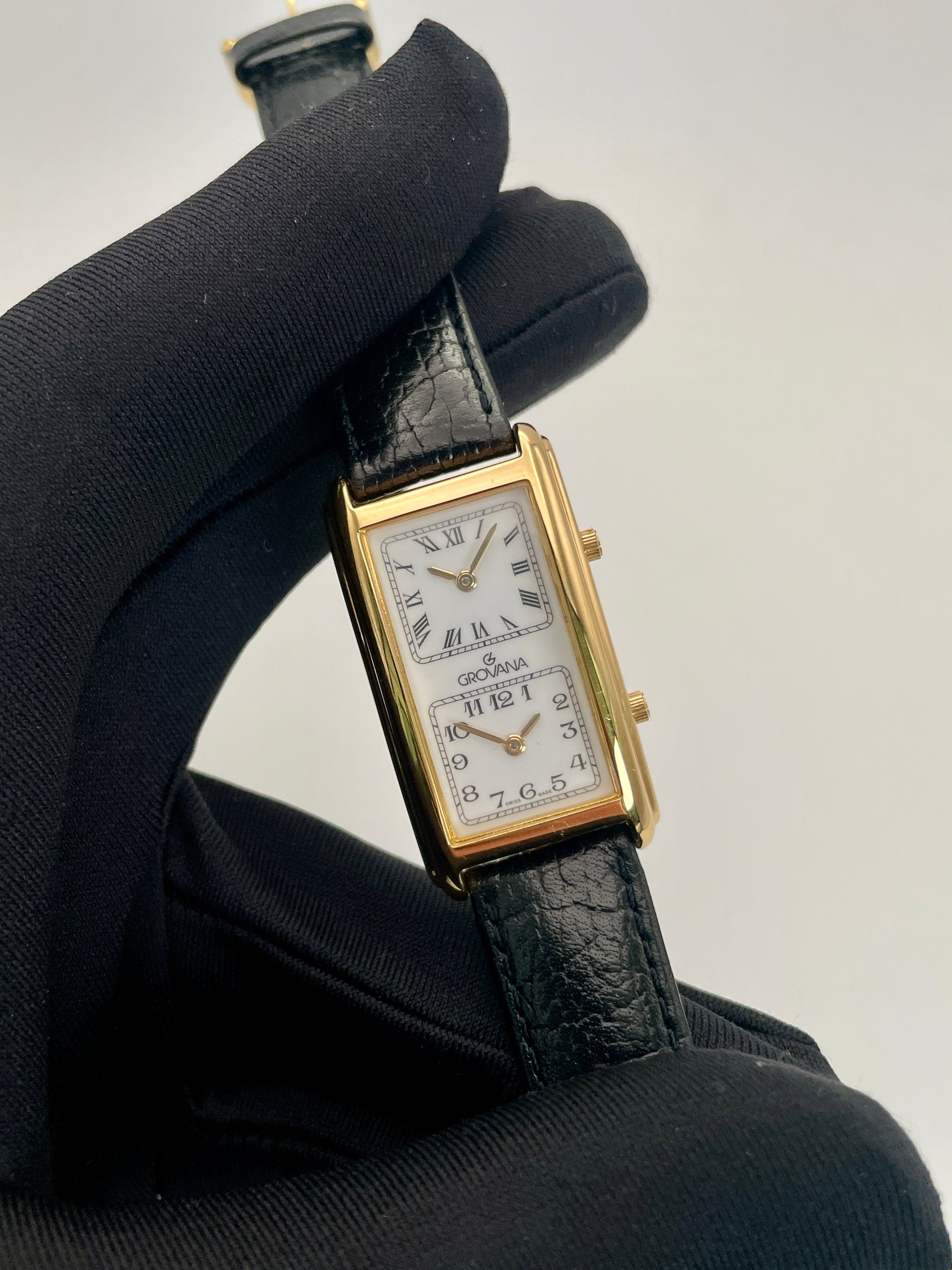 Close-up view of Grovana Tank Dual Time watch with a gold-tone rectangular case, white dual dials, and black leather strap.