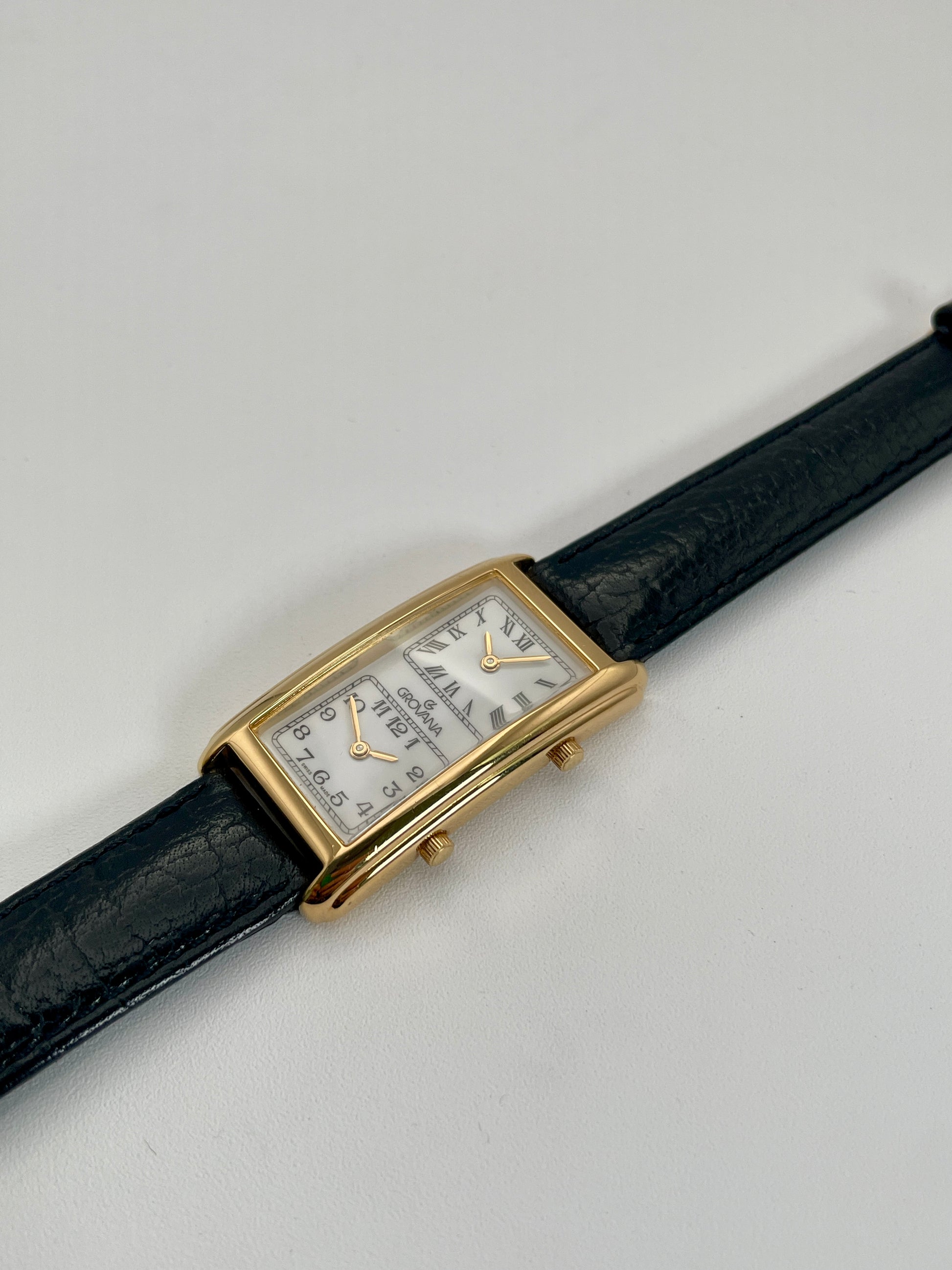 Diagonal view of Grovana Tank Dual Time watch highlighting the gold-tone rectangular case, white dual dials, and black leather strap.