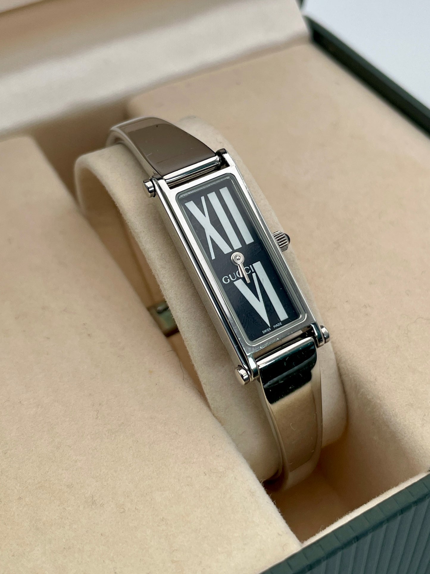 Gucci 1500L black dial watch with a rectangular silver-tone case and stainless steel bracelet, displayed in the original Gucci box.