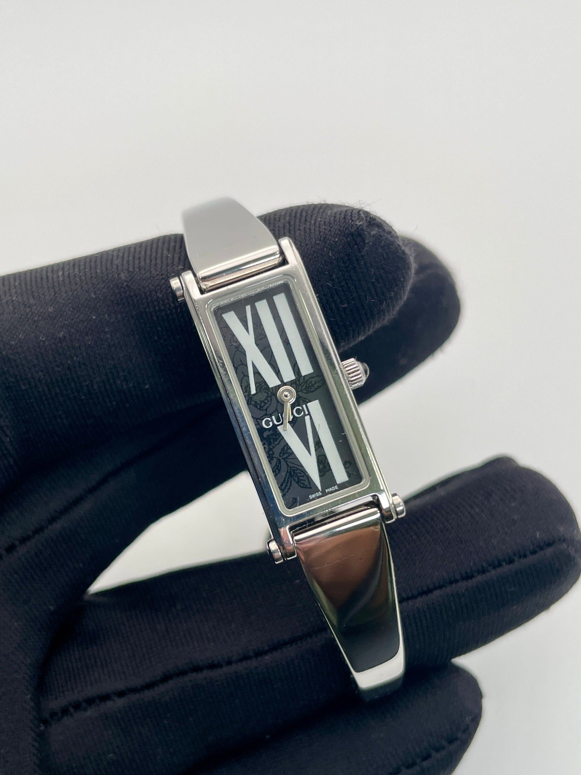 Close-up view of Gucci 1500L black dial watch with a rectangular silver-tone case, white dial, and stainless steel bracelet.