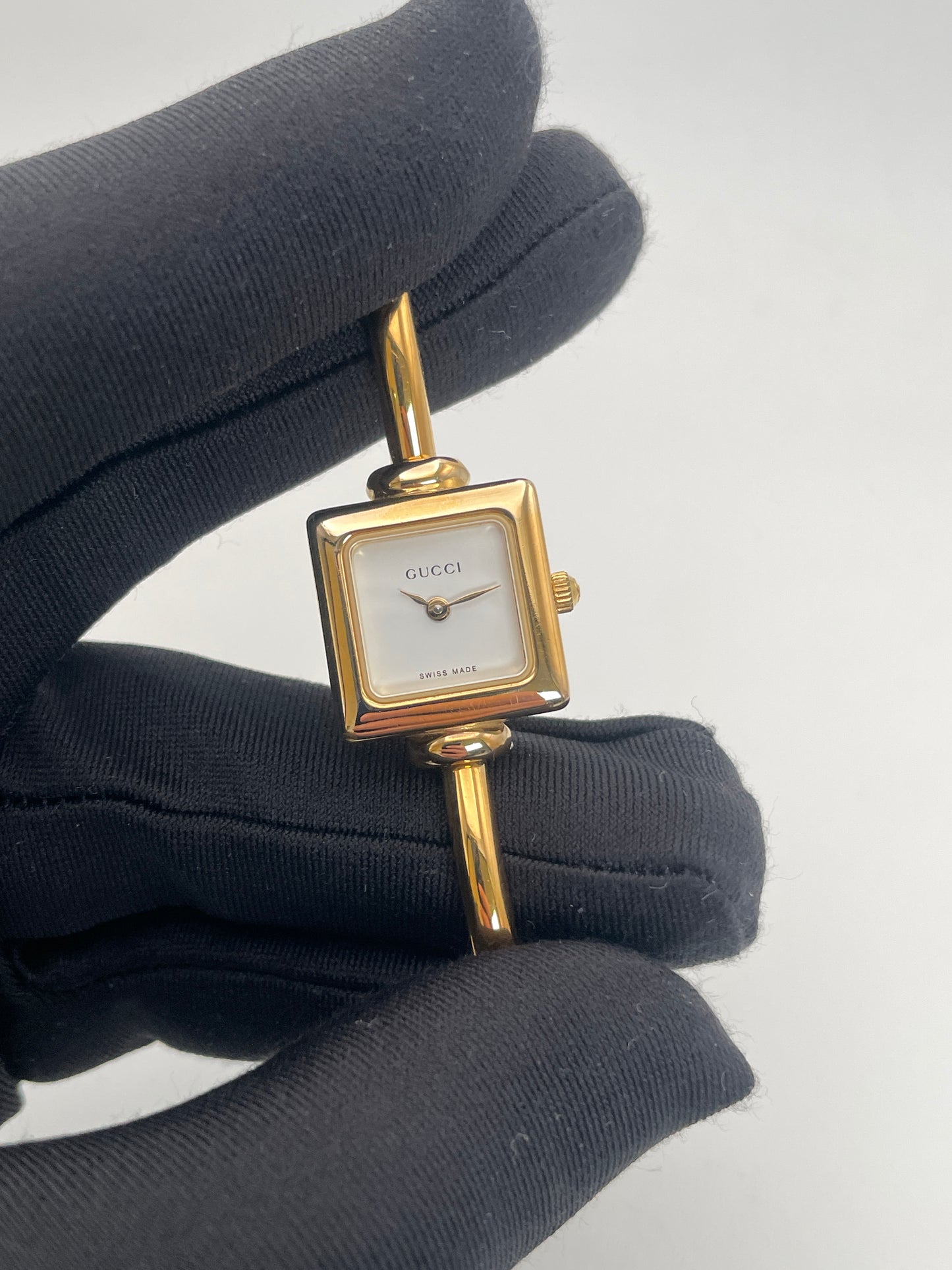 Close up view of Gucci 1900L gold watch with a square case and white dial, featuring a gold bangle bracelet.